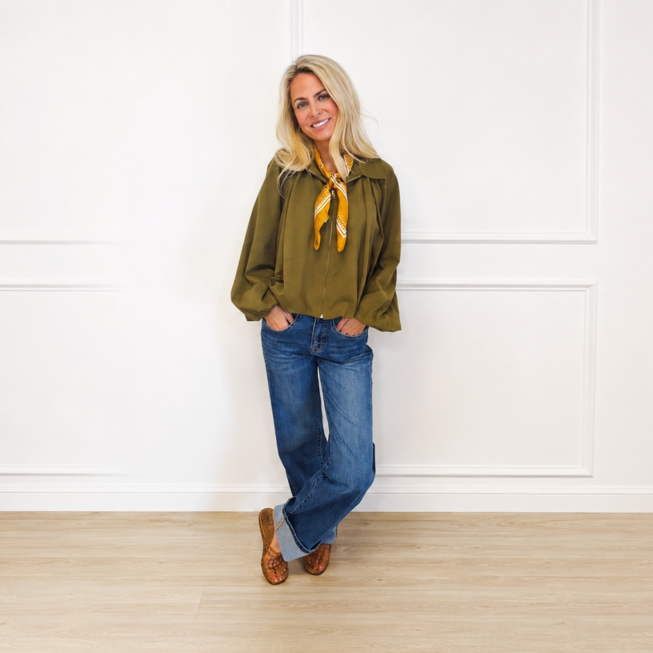 Woman wearing an olive zip-front jacket and cuffed wide-leg denim jeans in a bright white studio