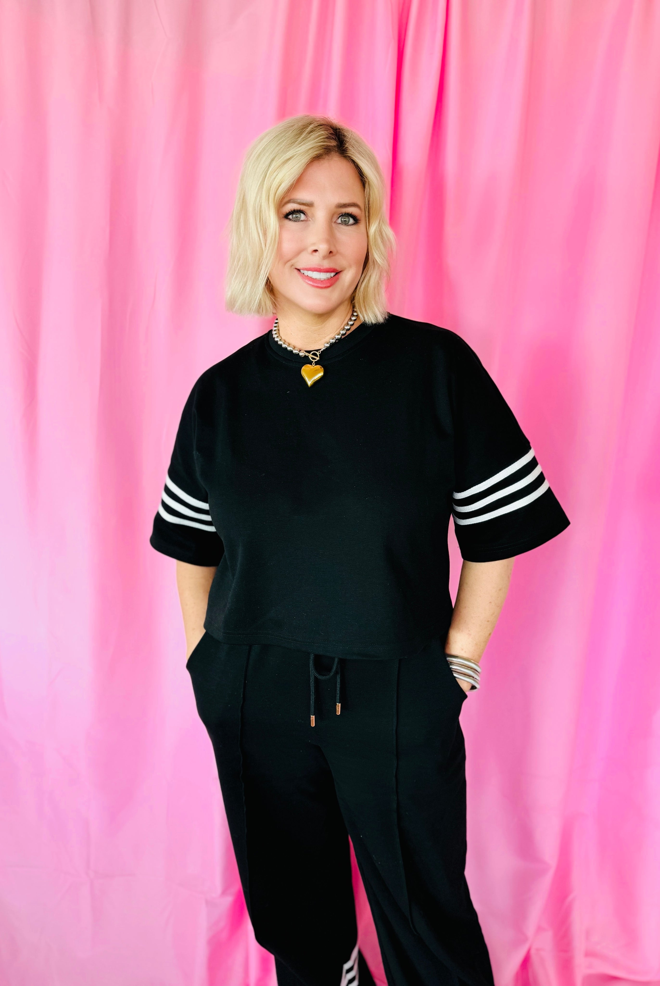 Black and white striped Entro matching set with cropped black top and black sweatpants. Model wears a gold heart necklace.