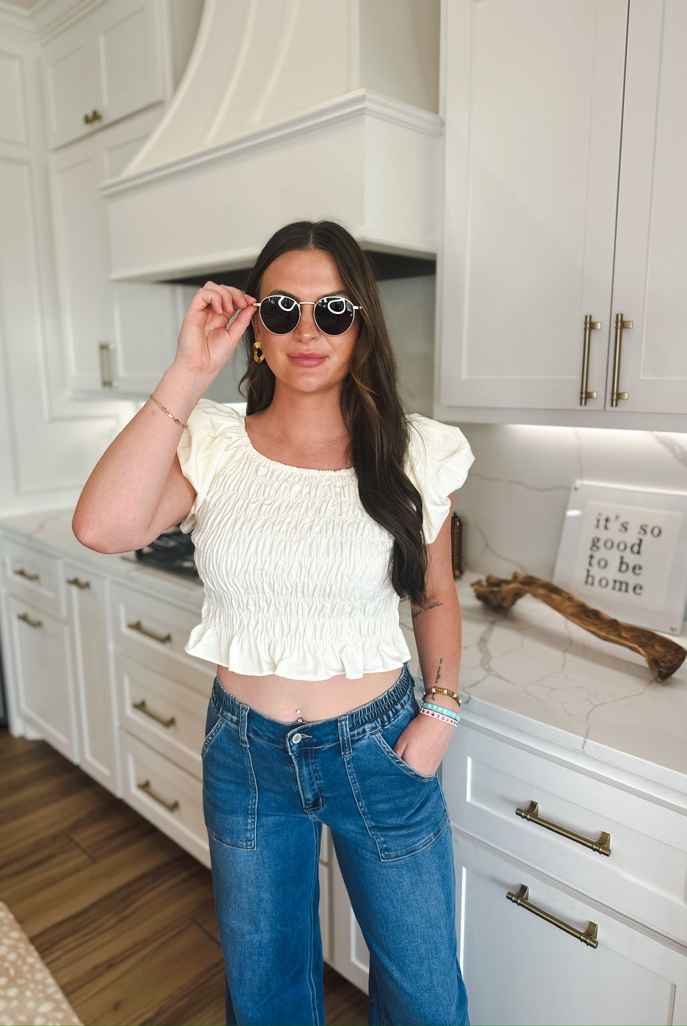 Woman wearing a soft yellow ruched puff sleeve crop top with blue denim jeans, accessorized with sunglasses and bracelets.
