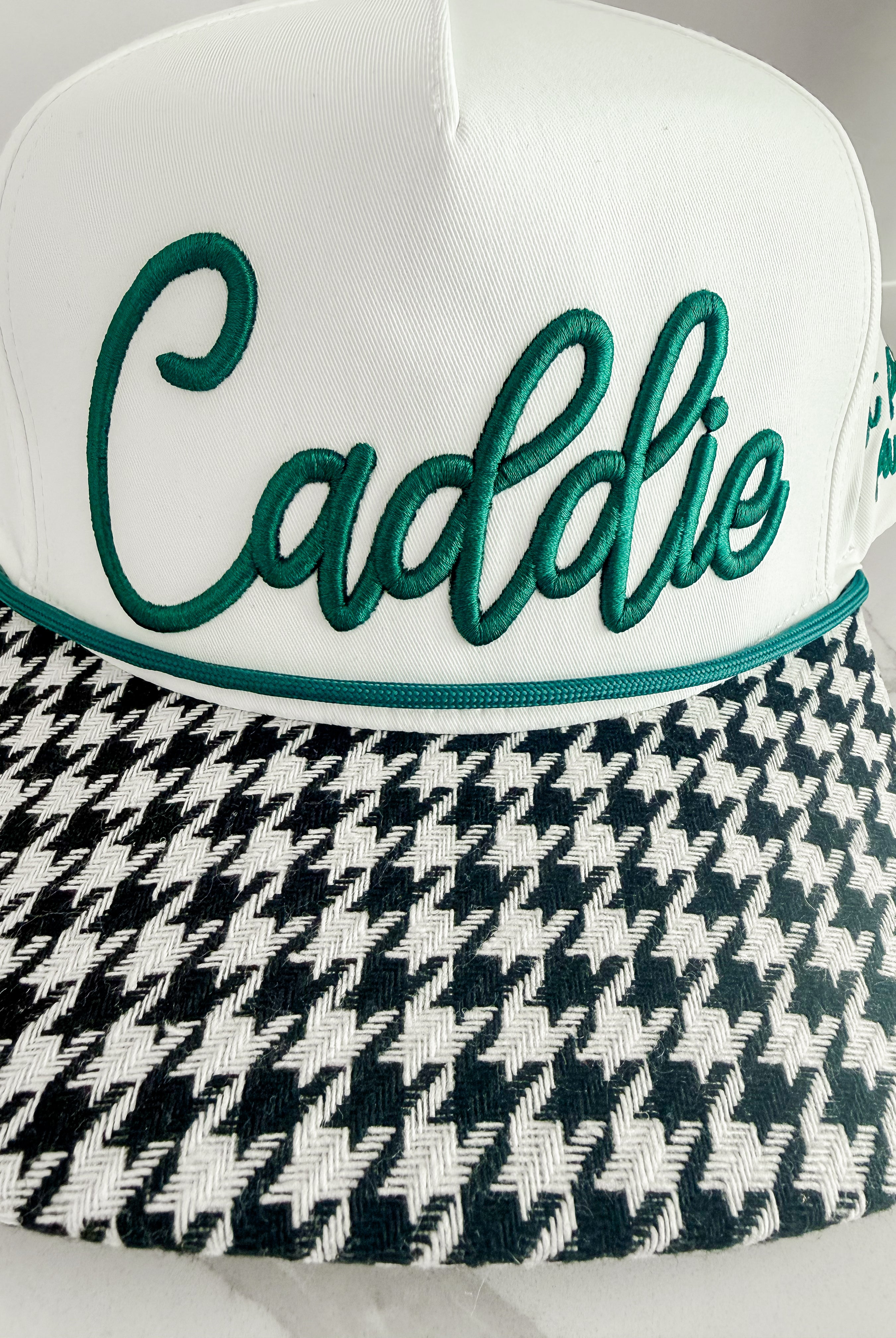 White caddie hat with green "Caddie" embroidery and black and white houndstooth brim.