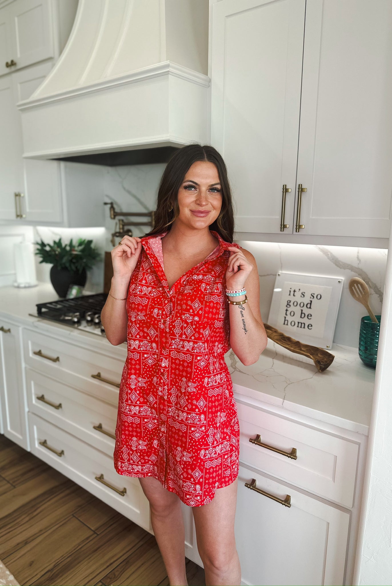 Red sleeveless romper with a white bandana print. A woman stands in a kitchen wearing the romper.