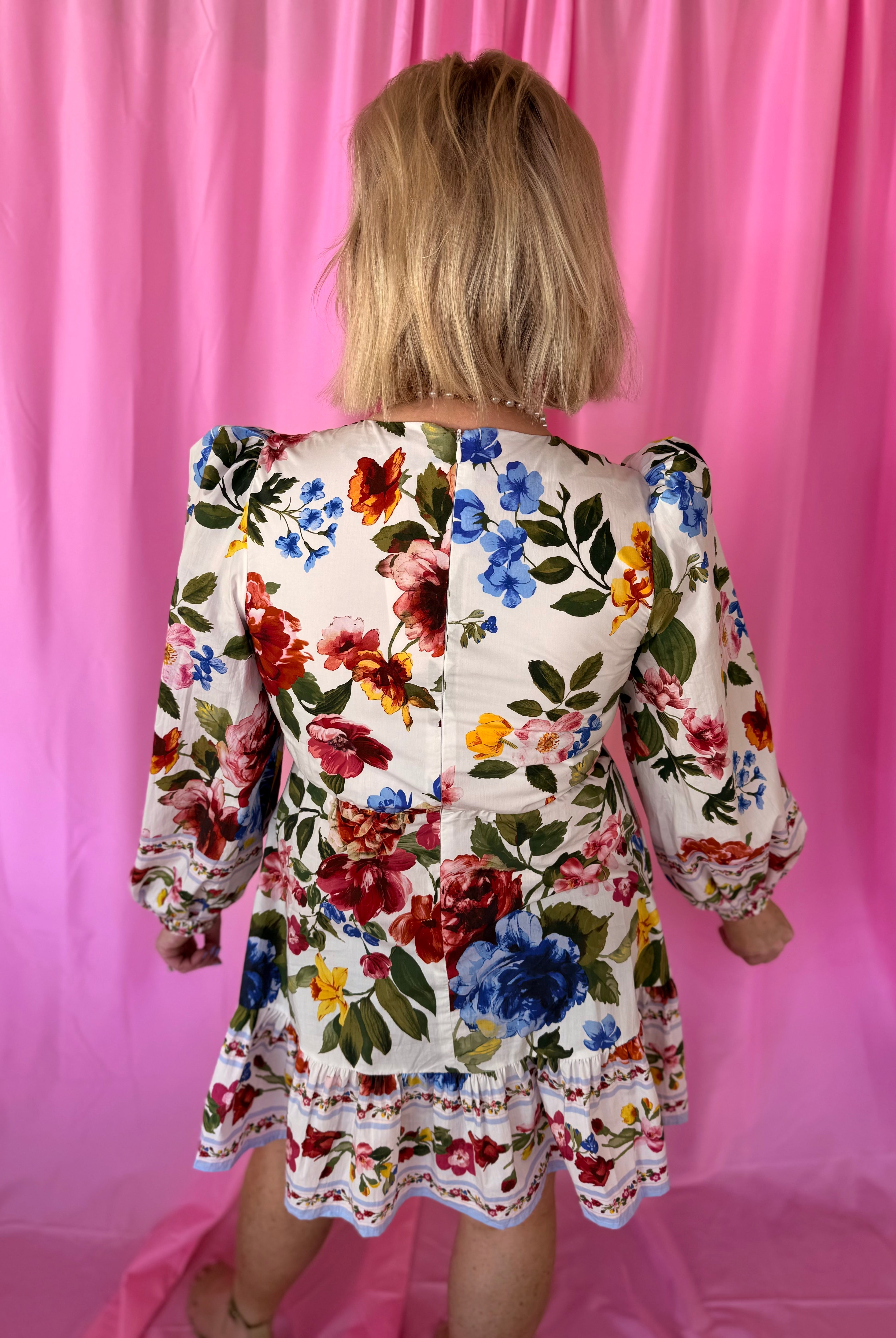 Back view of a white floral puff sleeve mini dress with red, blue, pink, yellow flowers and green leaves. Features a