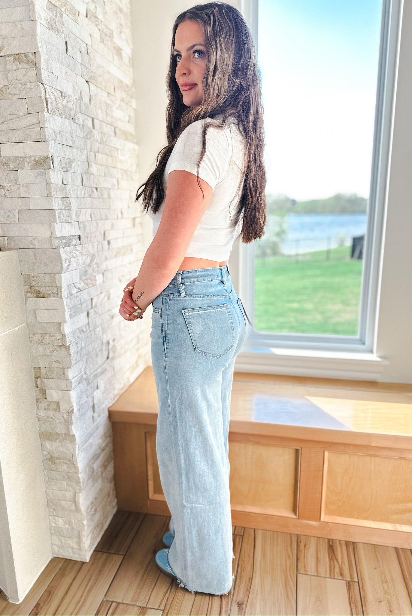 Woman in MICA LIGHT WASH WIDE LEG JEANS, featuring a light blue denim, high-waisted, and wide-leg silhouette with