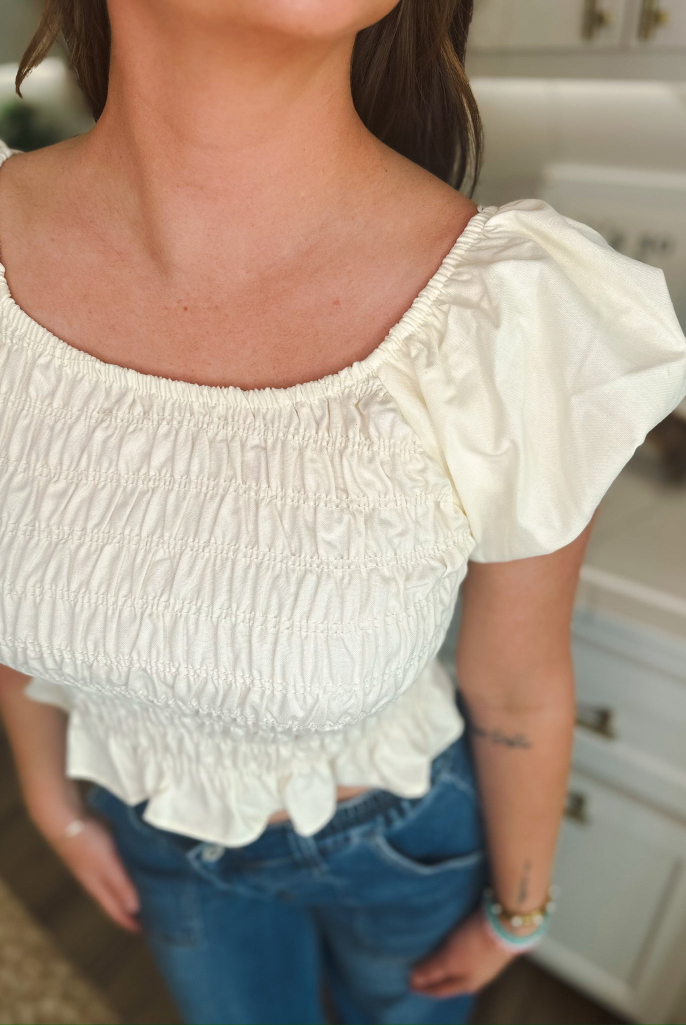 Cream puff sleeve ruched blouse with a square neckline, cinched waist, and ruffled hem, worn with blue jeans.
