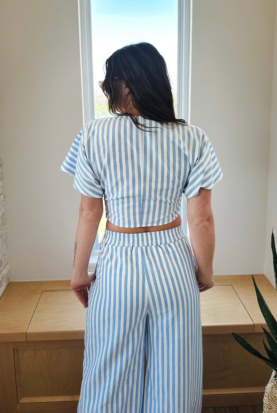 Back view of a woman wearing a blue and white striped twist front crop top and matching wide-leg pants set.