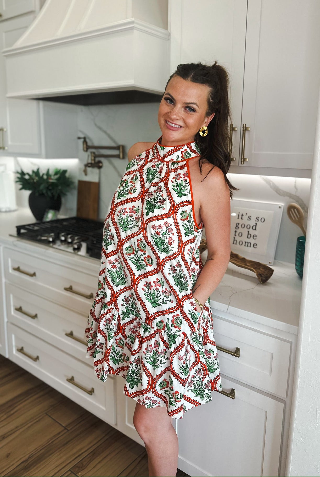Entro red and cream floral halter mini dress with ruffled hem. Woman wearing dress in a kitchen.