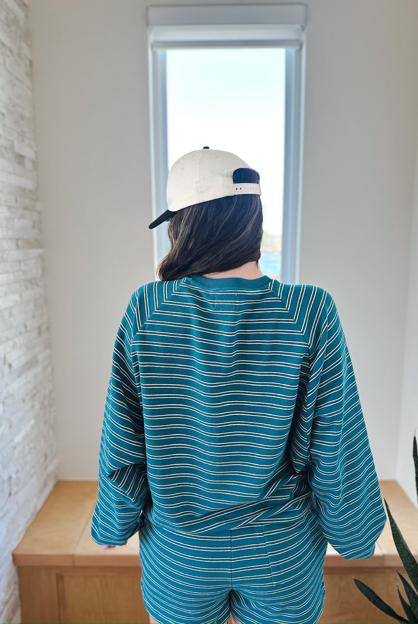 Teal and white striped long sleeve top and elastic waist shorts set worn by a person facing away, wearing a cream baseball