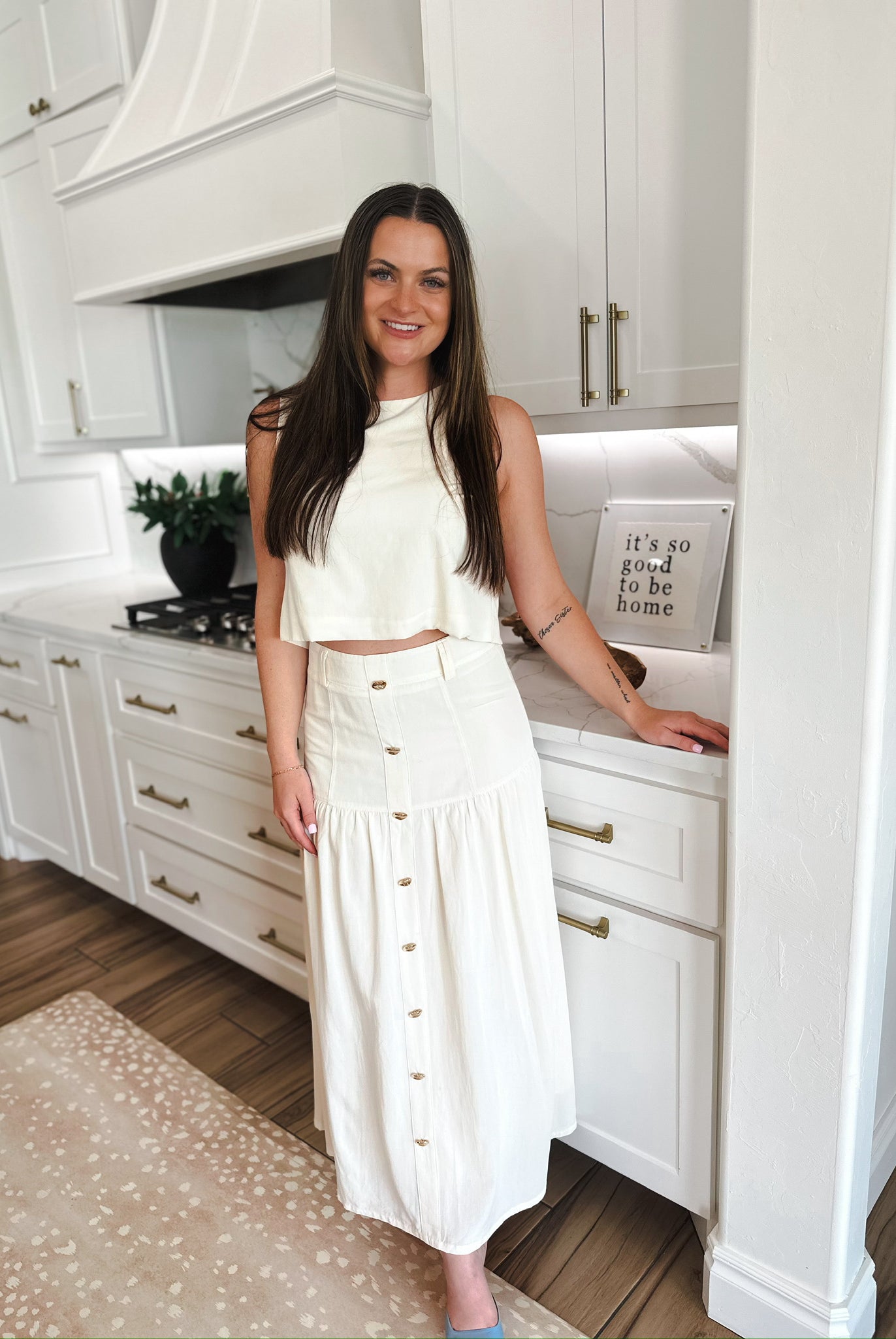 Woman wearing an elegant cream matching set: a cropped sleeveless top and a button-front midi skirt, standing in a modern