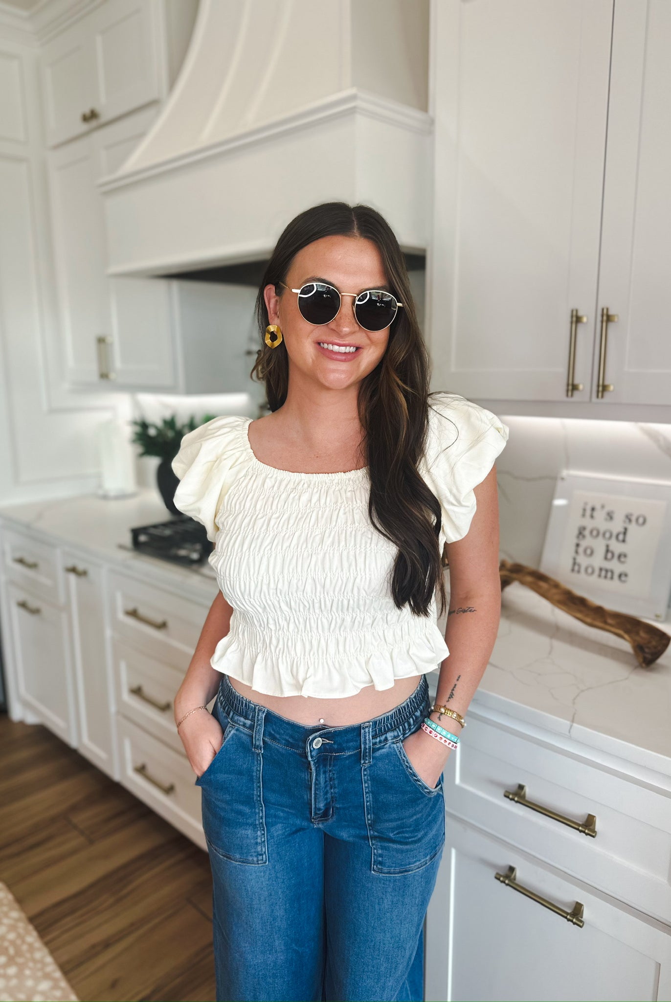 Woman wearing a soft yellow puff sleeve ruched blouse with a square neckline and a ruffled hem, paired with blue denim