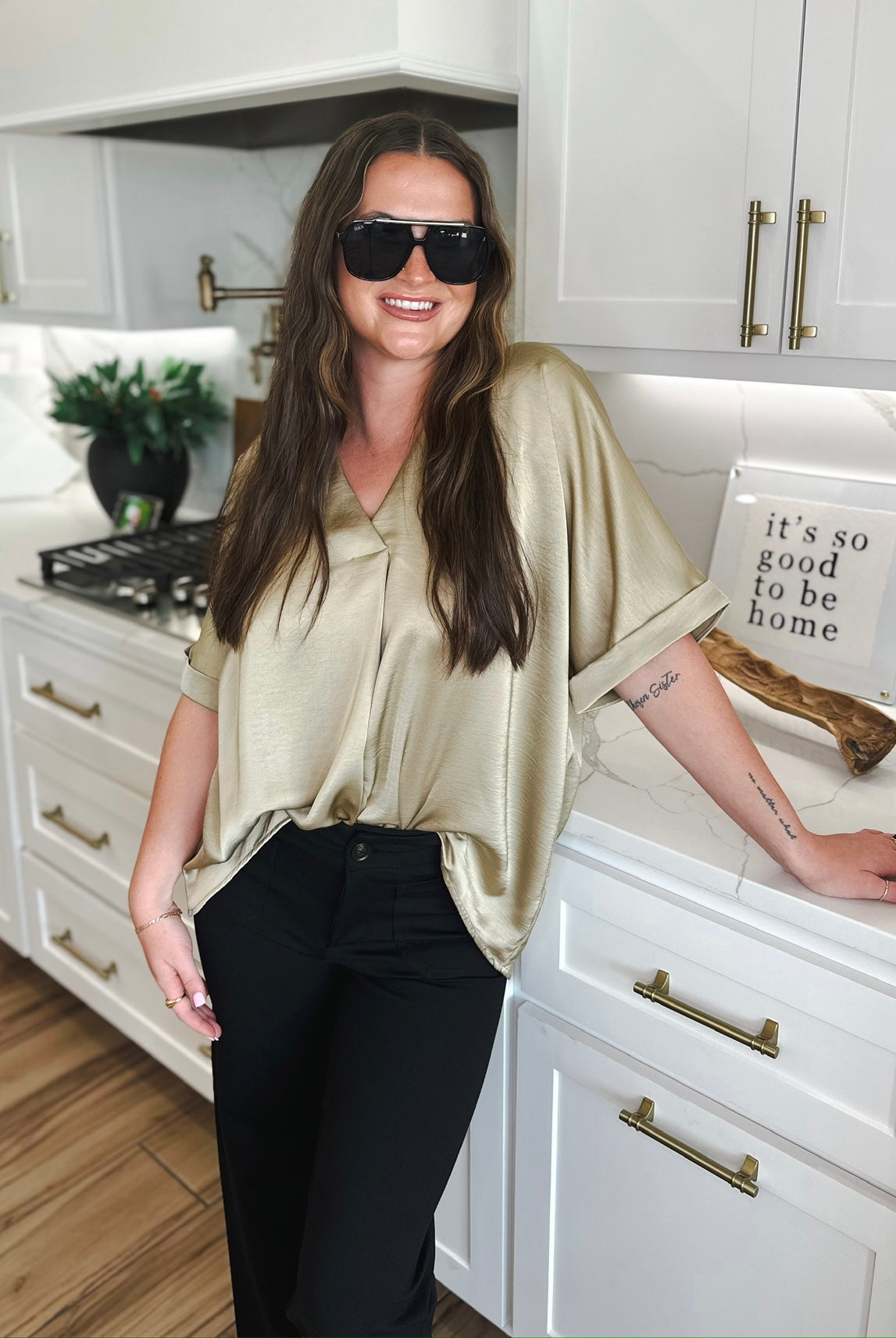 Woman in taupe satin V-neck blouse and black pants, wearing sunglasses.