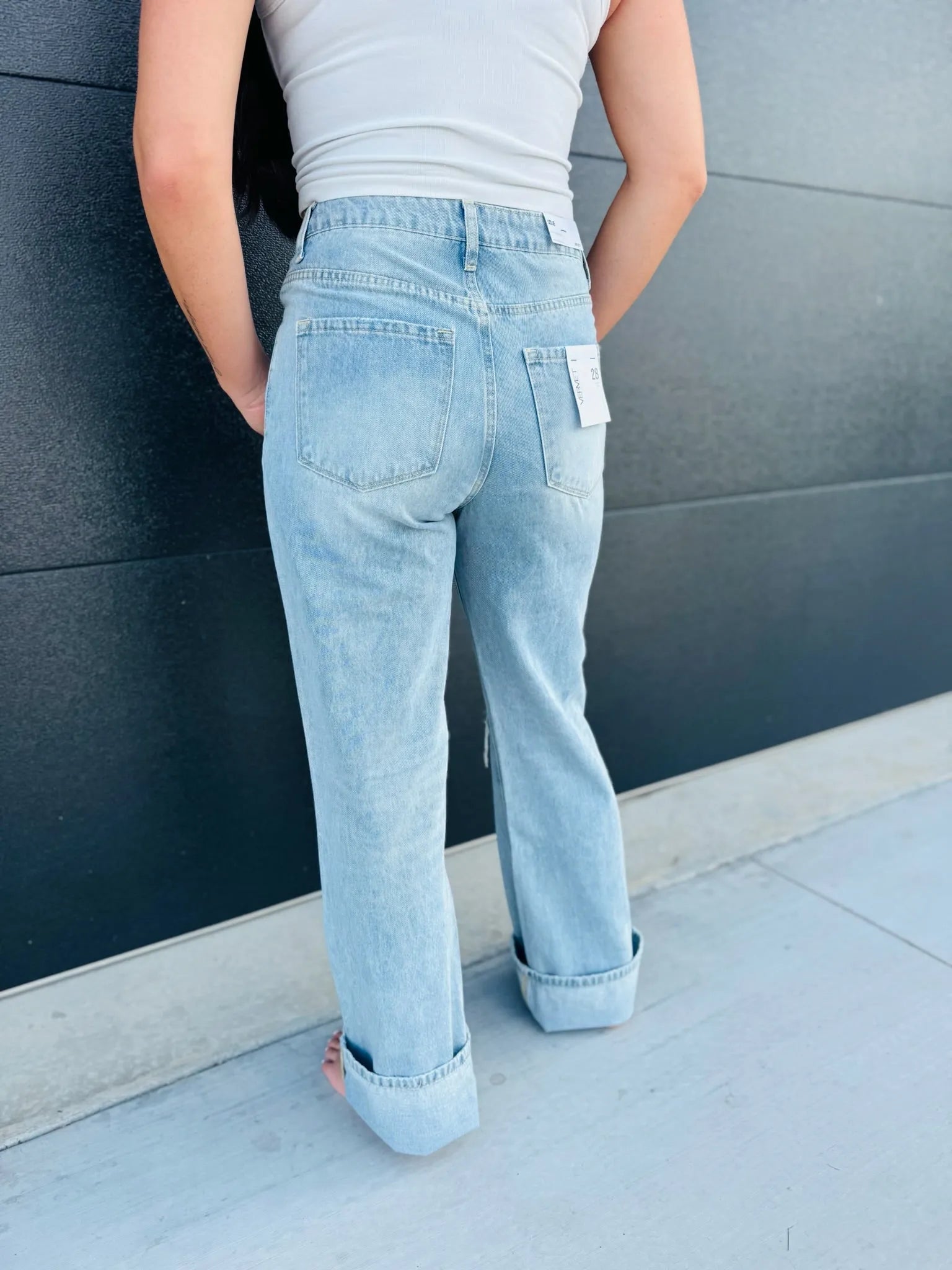 Back view of a person wearing light wash, super high rise flare jeans with large cuffs and a white tank top.