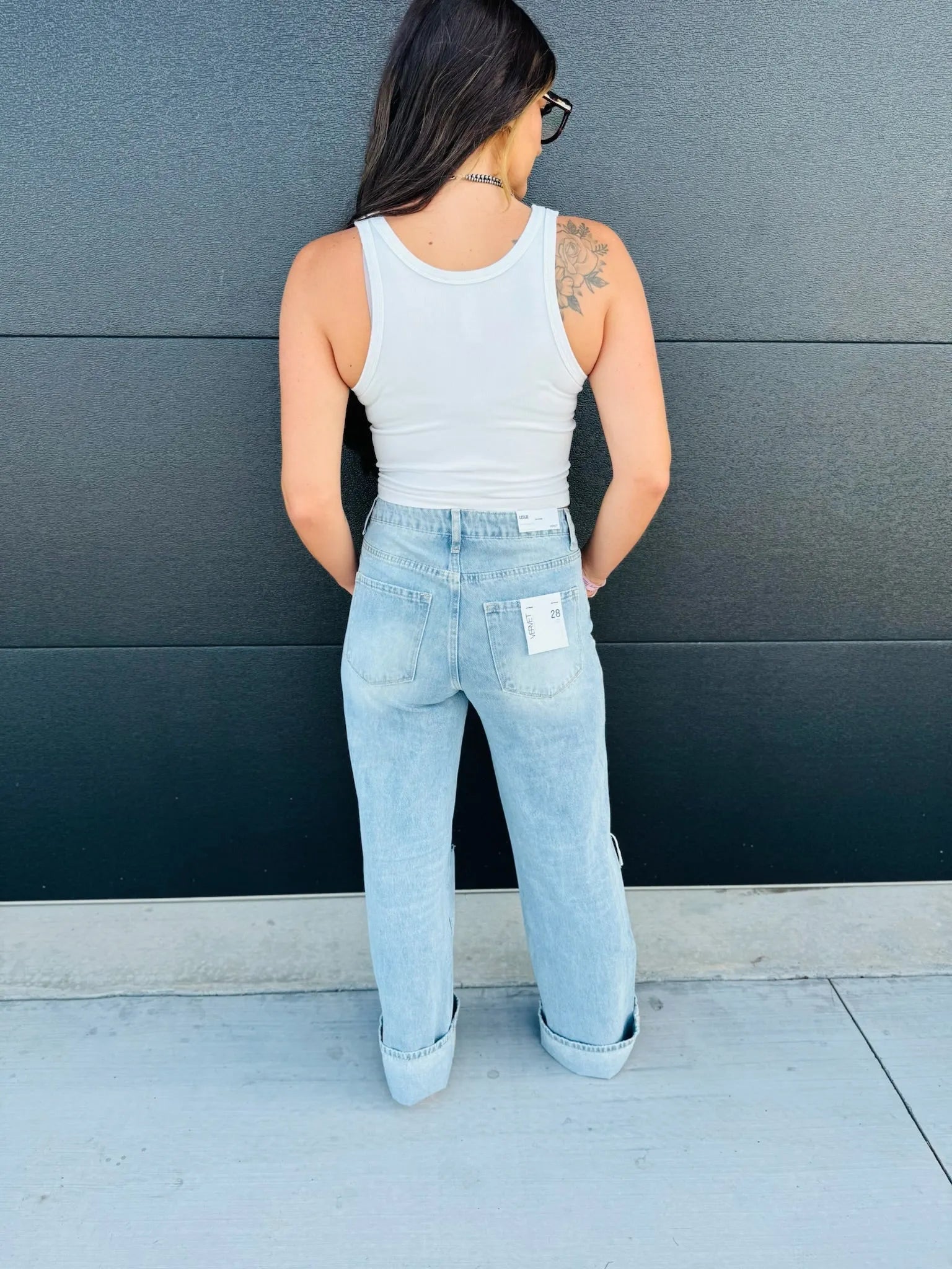 Back view of a woman wearing light wash, super high rise flare jeans with rolled cuffs and a white tank top. Jeans have a