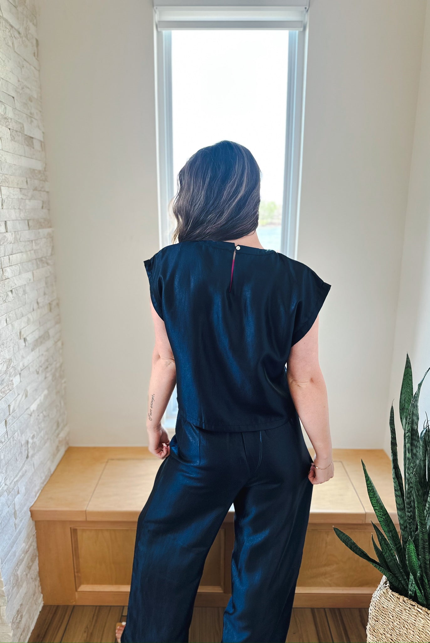 Back view of a woman wearing a navy shimmer short sleeve top and matching wide-leg pants. The top has a button closure at