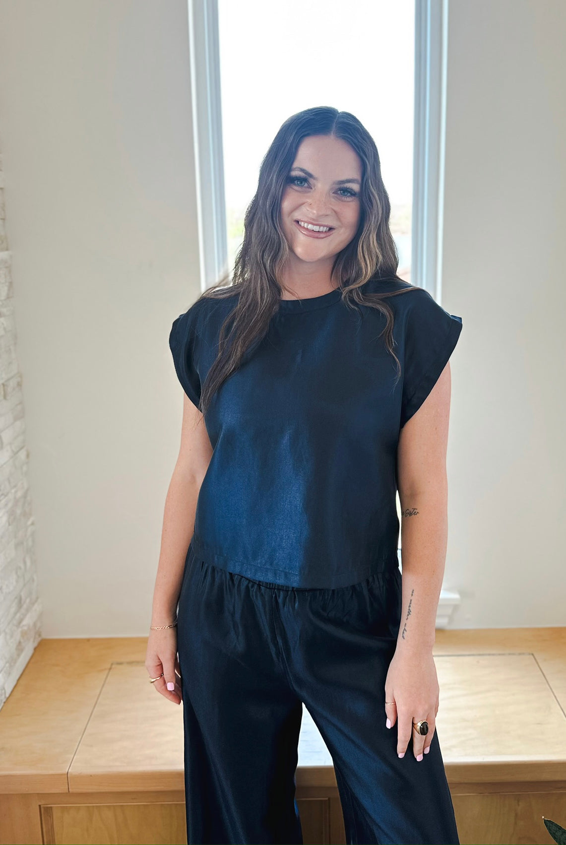 Woman smiling, wearing a navy shimmer short sleeve top with ruffled hem and matching wide-leg pants.