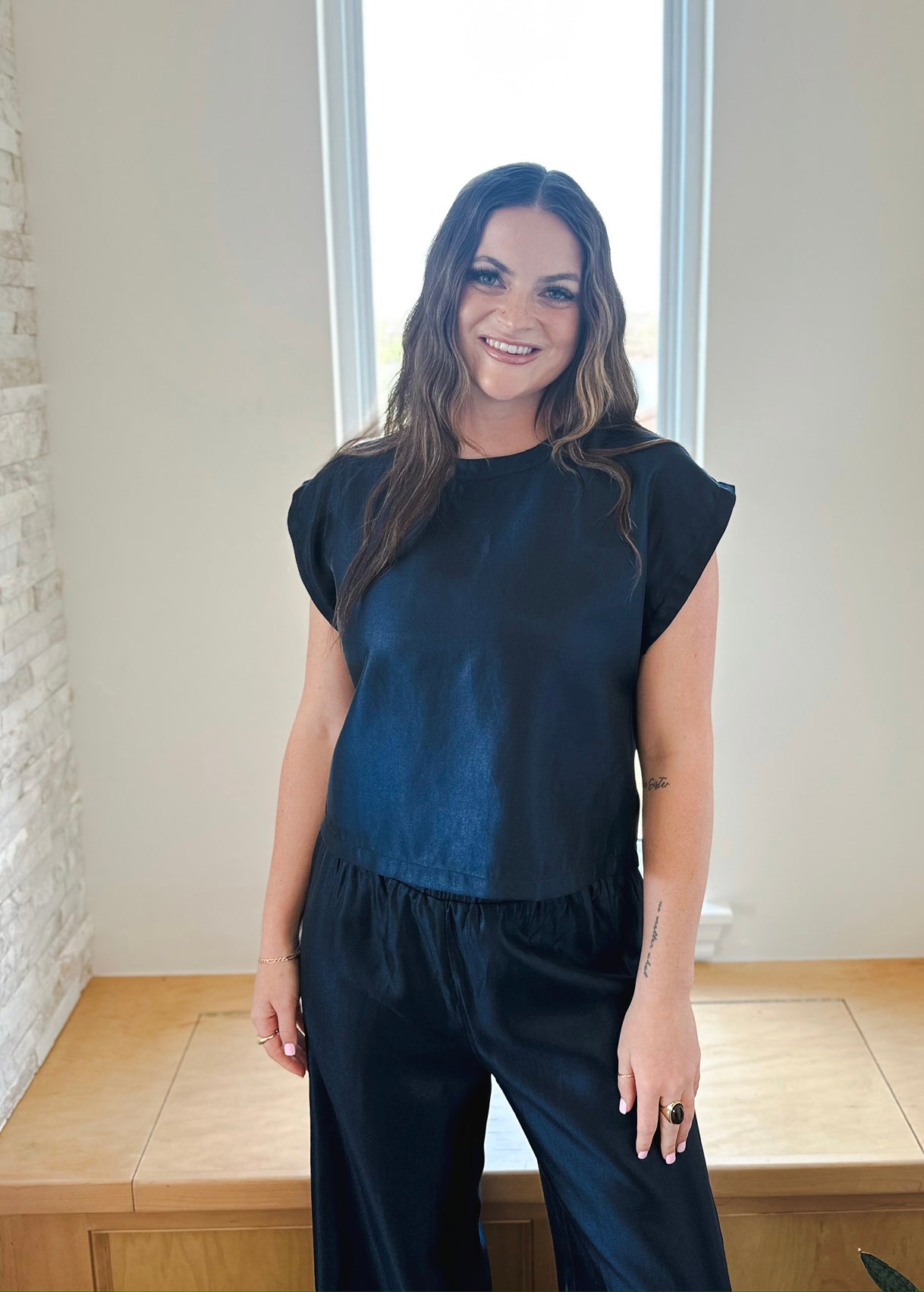 Woman smiling, wearing a navy shimmer short sleeve top with ruffled hem and matching wide-leg pants.