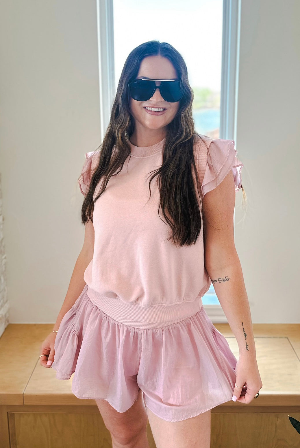 Light pink athleisure set featuring a ruffled sleeve pullover and crinkle nylon shorts on a woman wearing sunglasses.