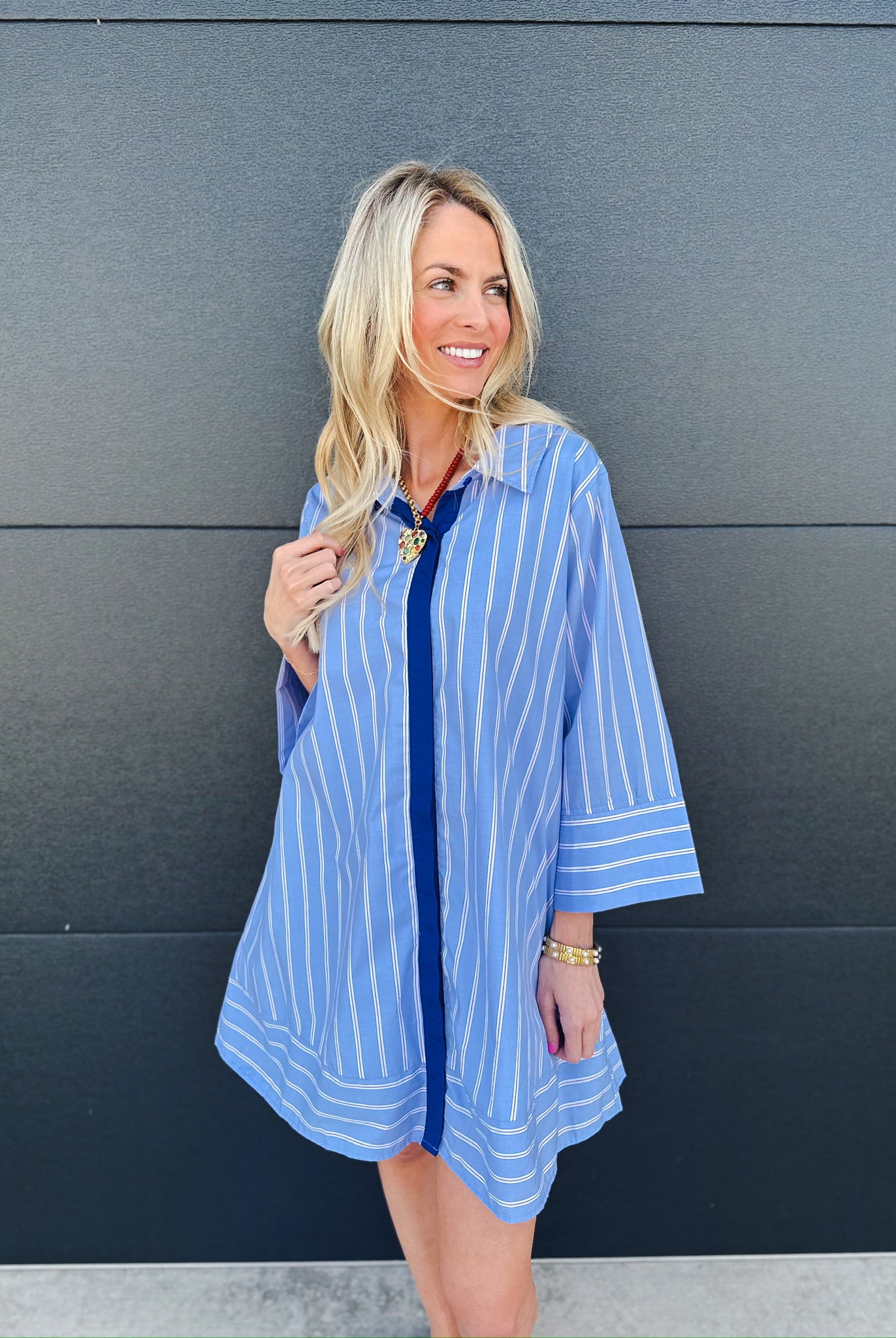 Woman wearing an Entro blue and white vertical striped button up shirt dress with wide sleeves and a dark blue placket.