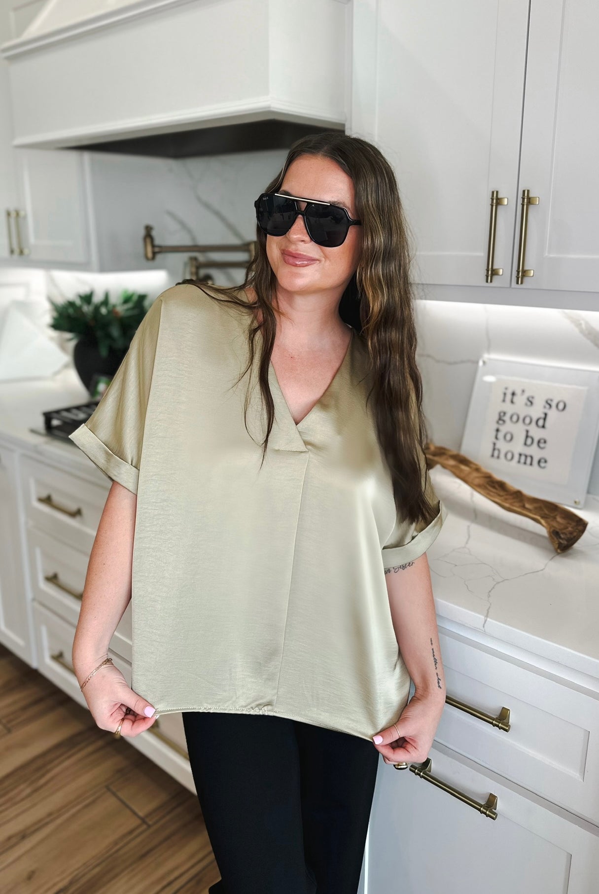 Taupe satin V-neck blouse with cuffed short sleeves, shown on a woman in a modern kitchen.