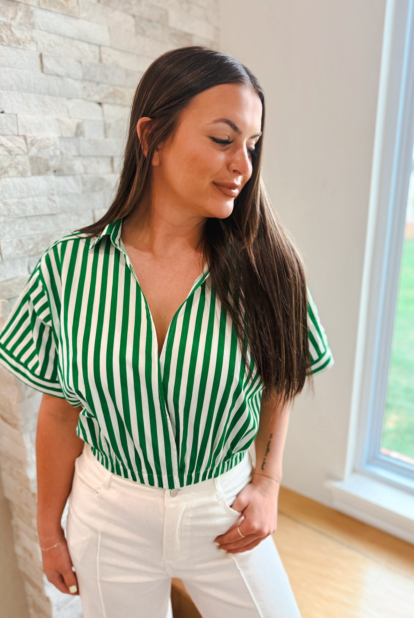 Woman wearing a green and white striped V-neck crop top with lapel collar and short sleeves, paired with white pants.
