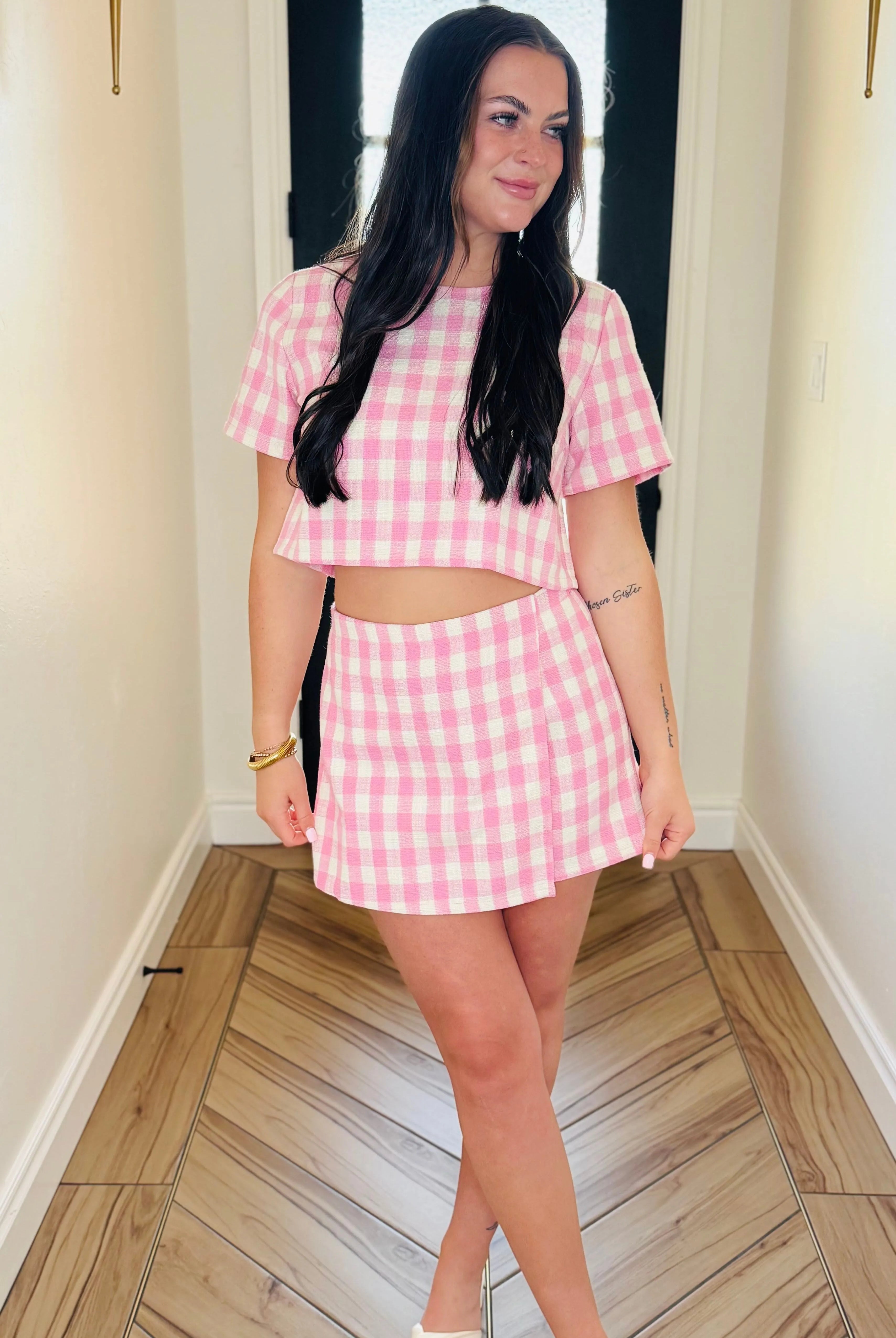 Pink gingham tweed skort set with short sleeves and a mini skirt. Model wears a gold bracelet and white sandals.