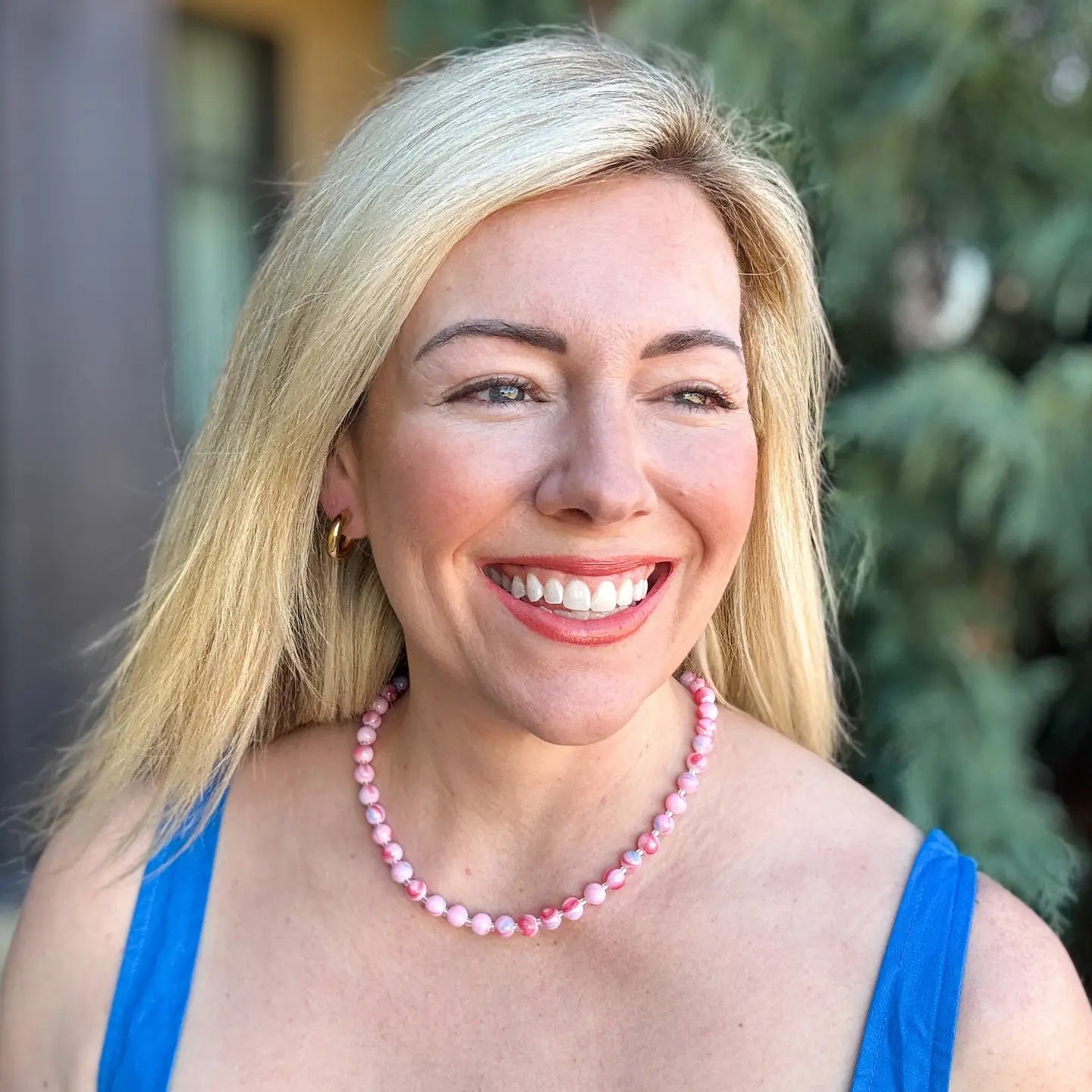 Woman wearing a pink beaded necklace and a blue top, smiling.