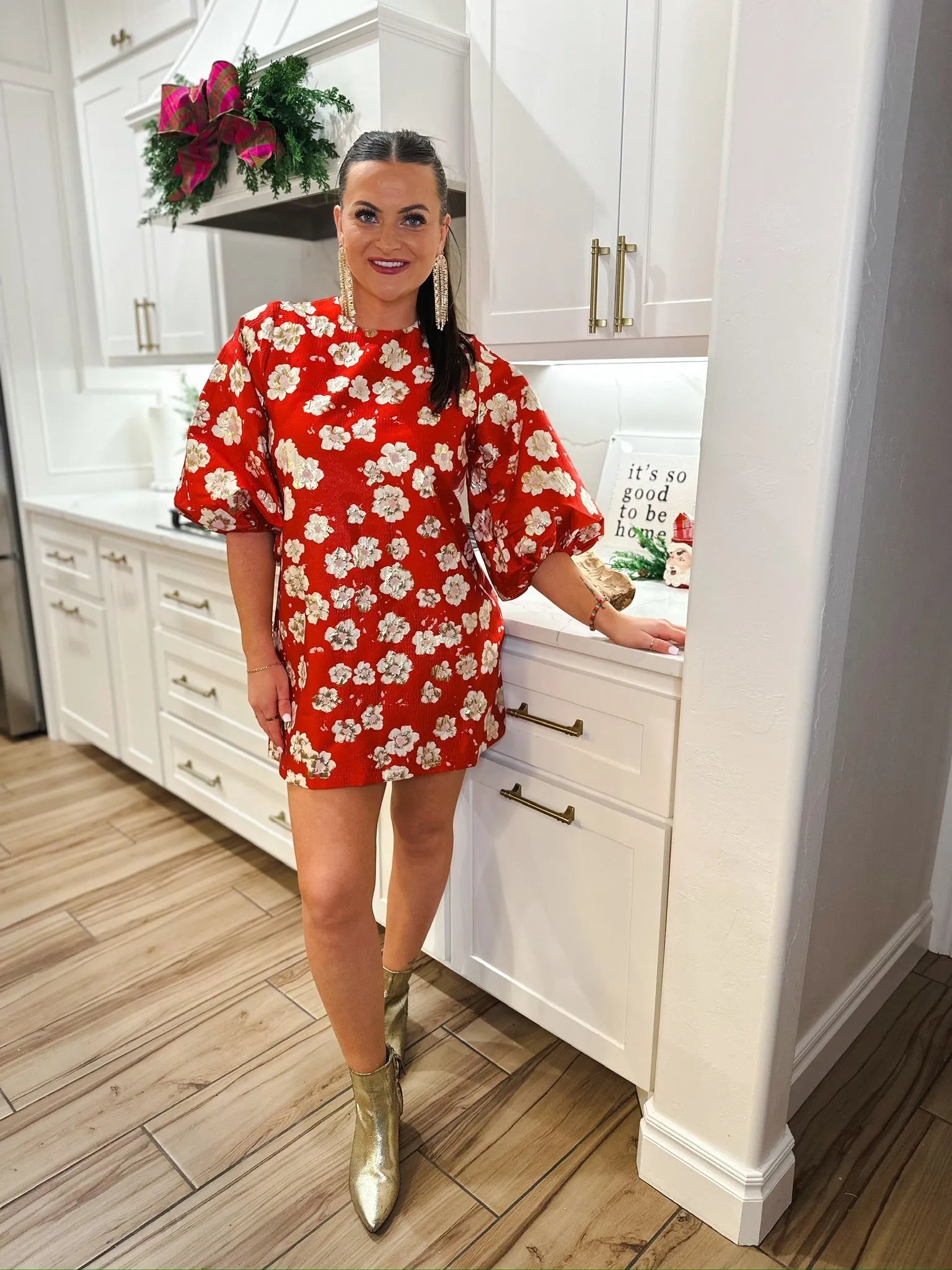 Woman in a red jacquard short dress with a white floral print, puff sleeves, and gold ankle boots.