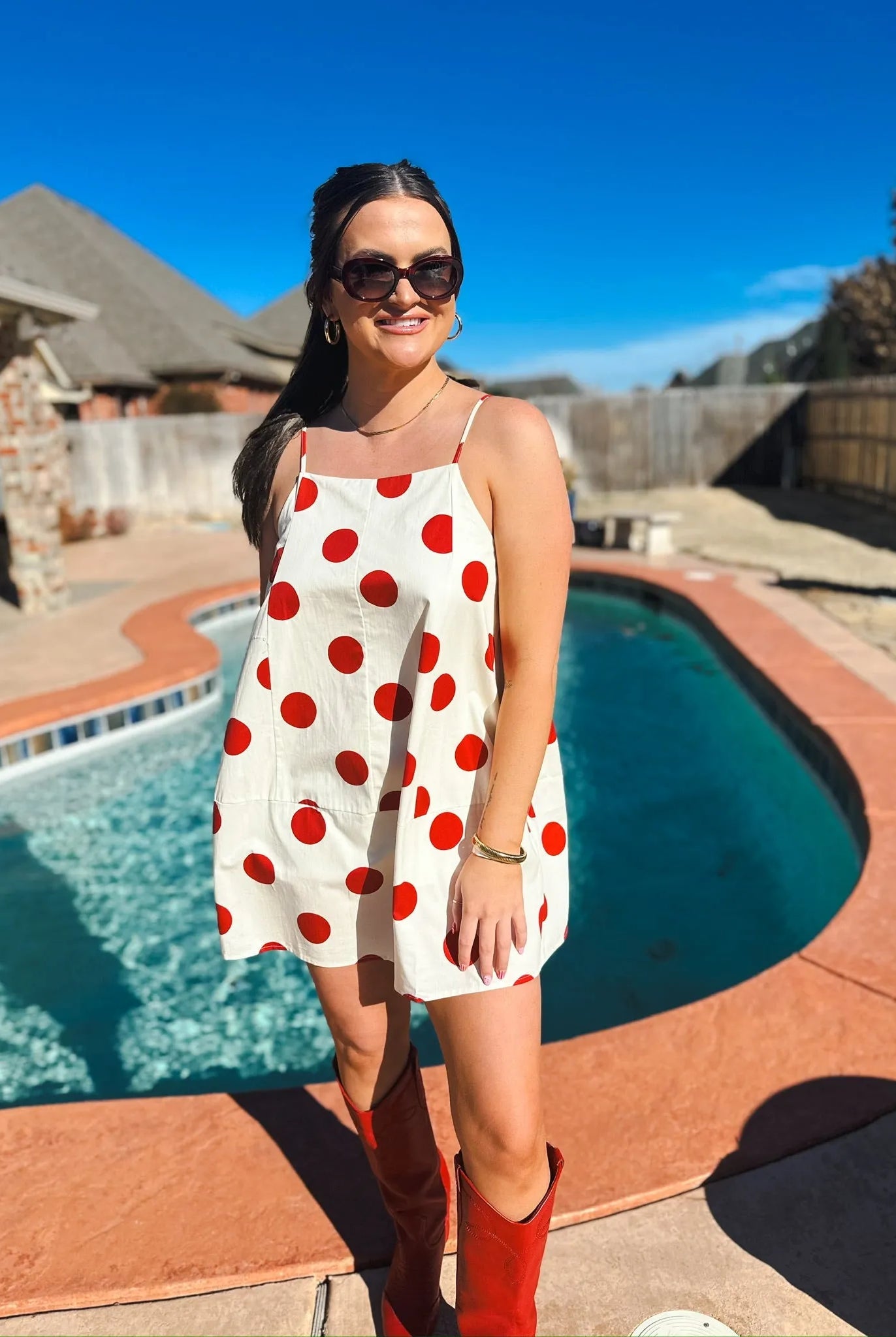 Woman in a cream mini dress with big red polka dots, spaghetti straps, and red cowboy boots.