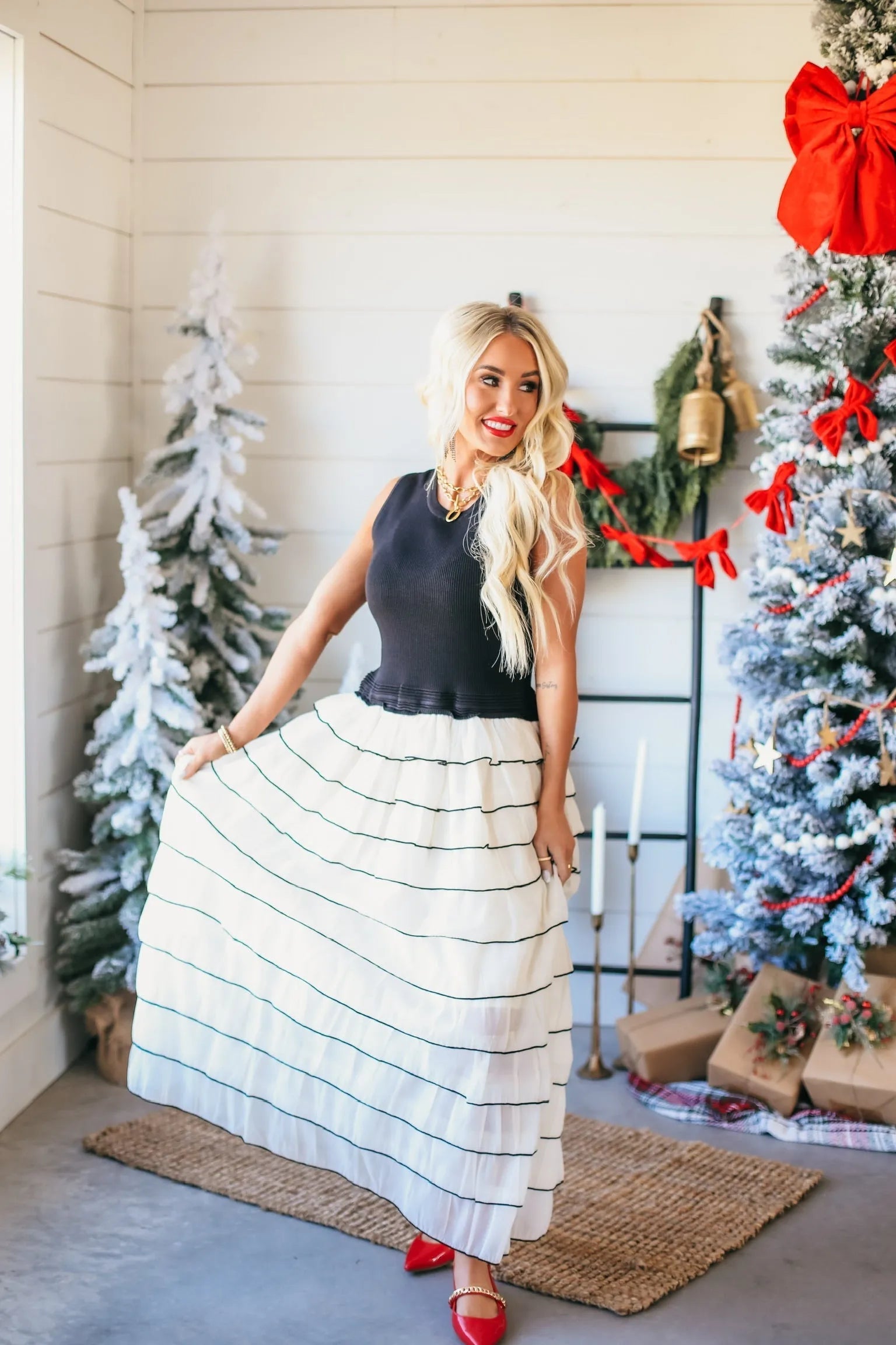 Woman in black and ivory ruffled dress with black stripes, standing by a decorated Christmas tree.