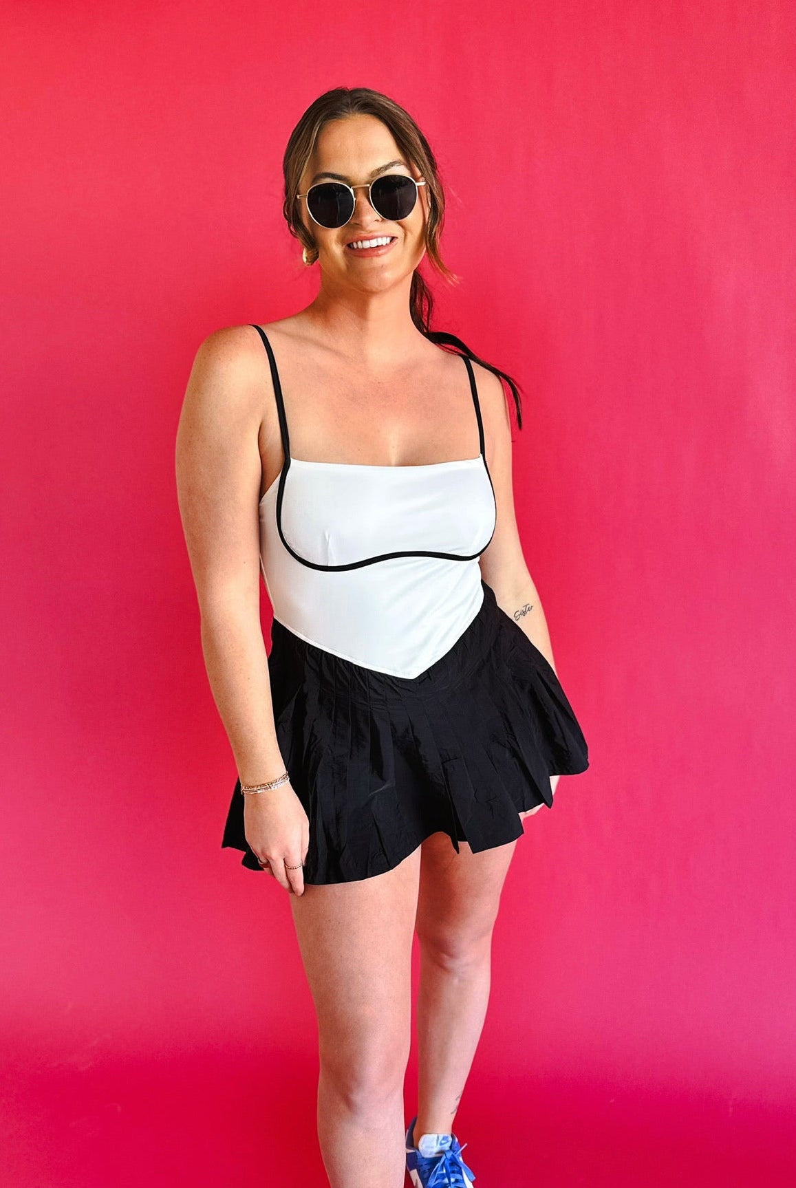 Black & white colorblock athletic dress with spaghetti straps and a pleated skirt. Model wears sunglasses and blue sneakers.