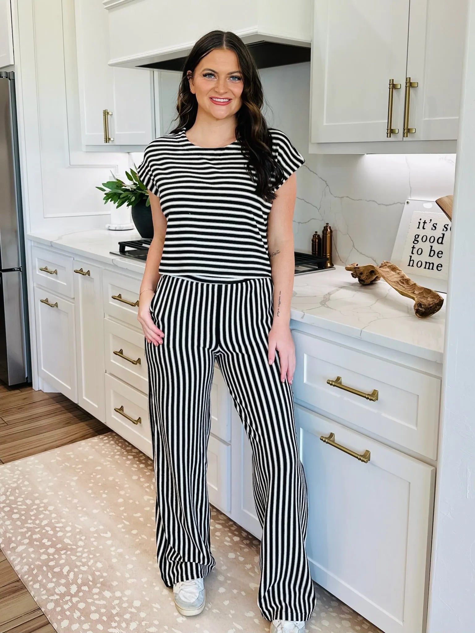Woman in black and white striped knit top and matching wide-leg pants, standing in a kitchen.