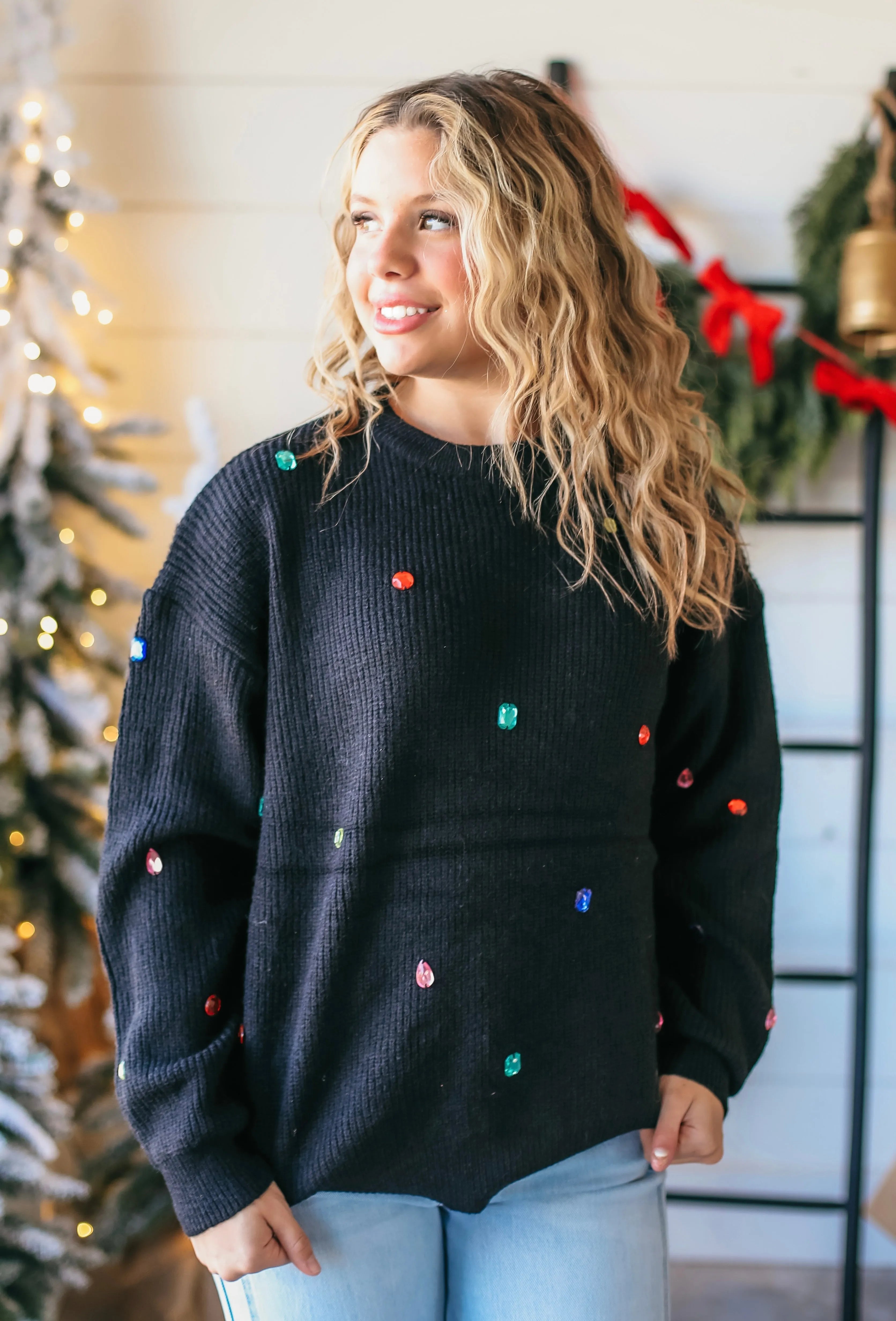 Black crewneck sweater with scattered multi-color jewels. Ribbed knit texture. Perfect for festive occasions.