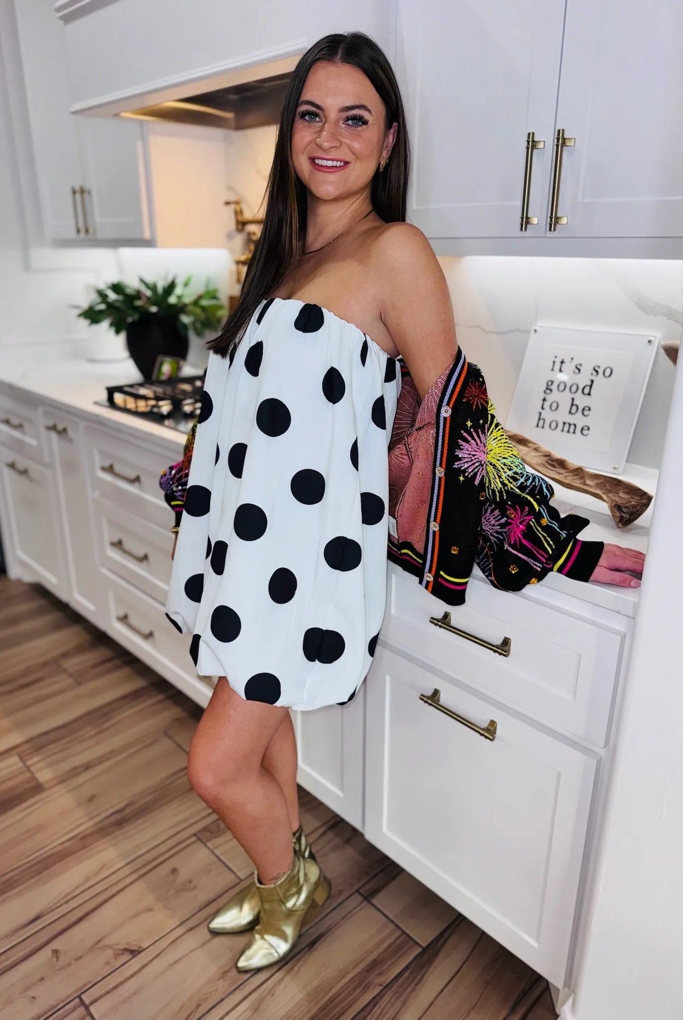 Woman wearing a black and white polka dot bubble dress and gold boots in a kitchen.