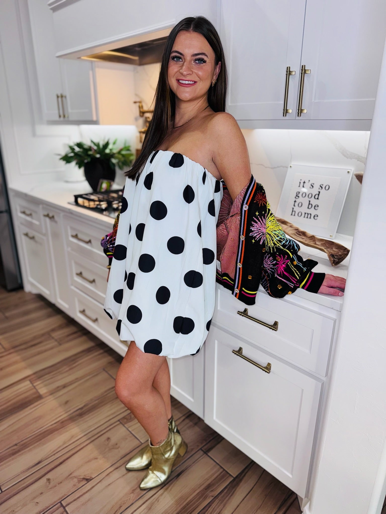 Woman wearing a black and white polka dot bubble dress and gold boots in a kitchen.
