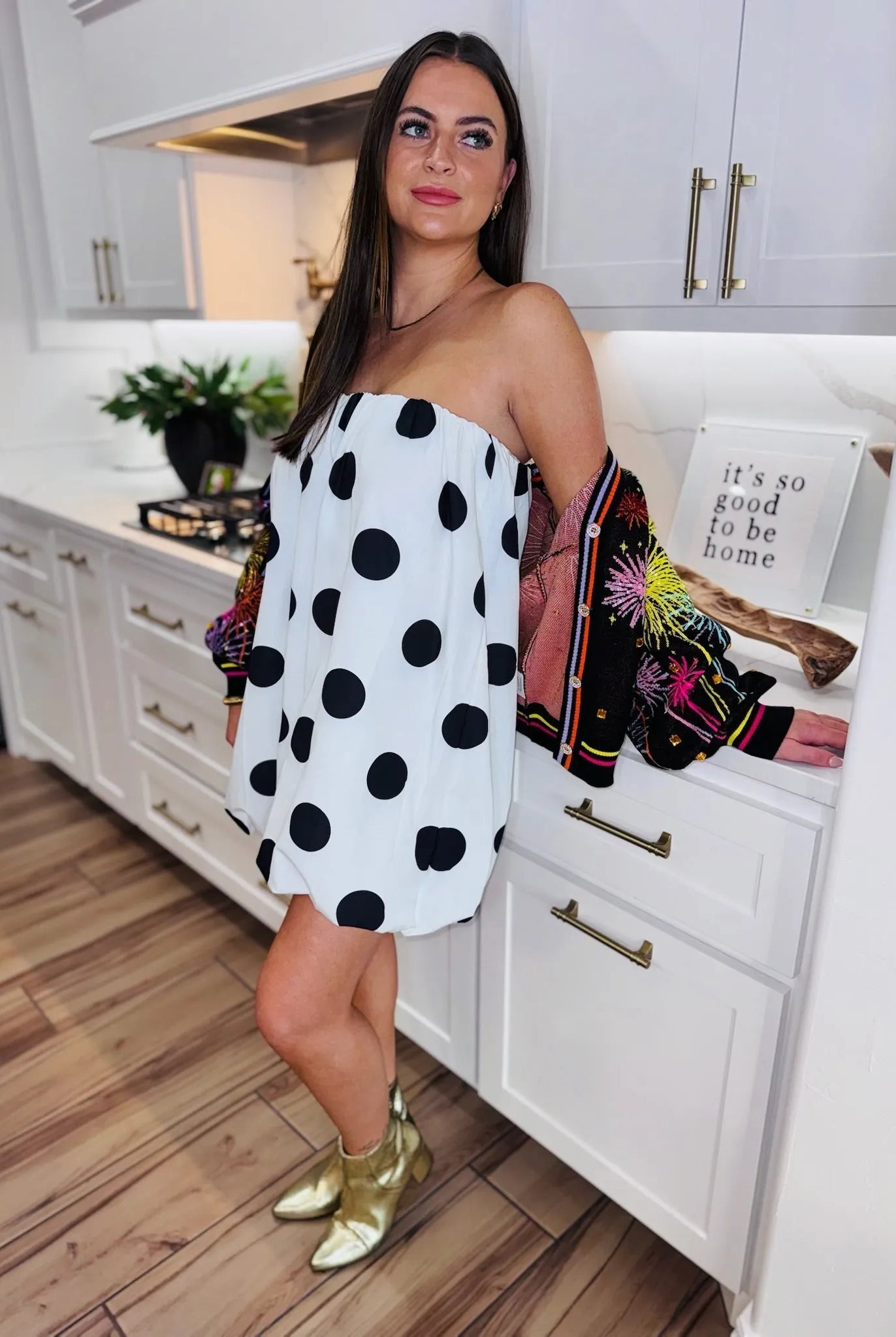 Woman wearing a black and white polka dot bubble dress and gold boots, with a colorful embroidered jacket.