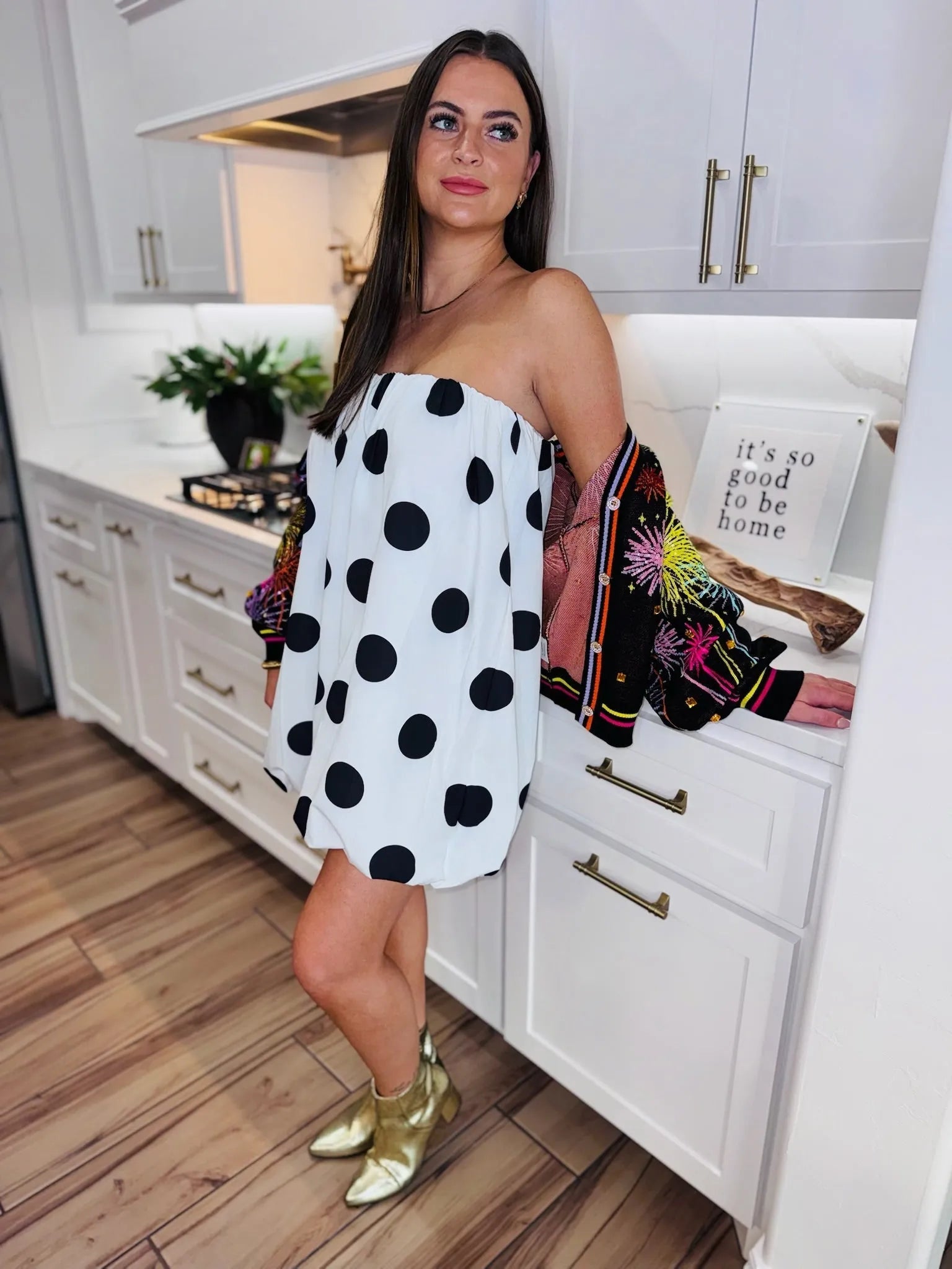 Woman wearing a black and white polka dot bubble dress and gold boots, with a colorful embroidered jacket.