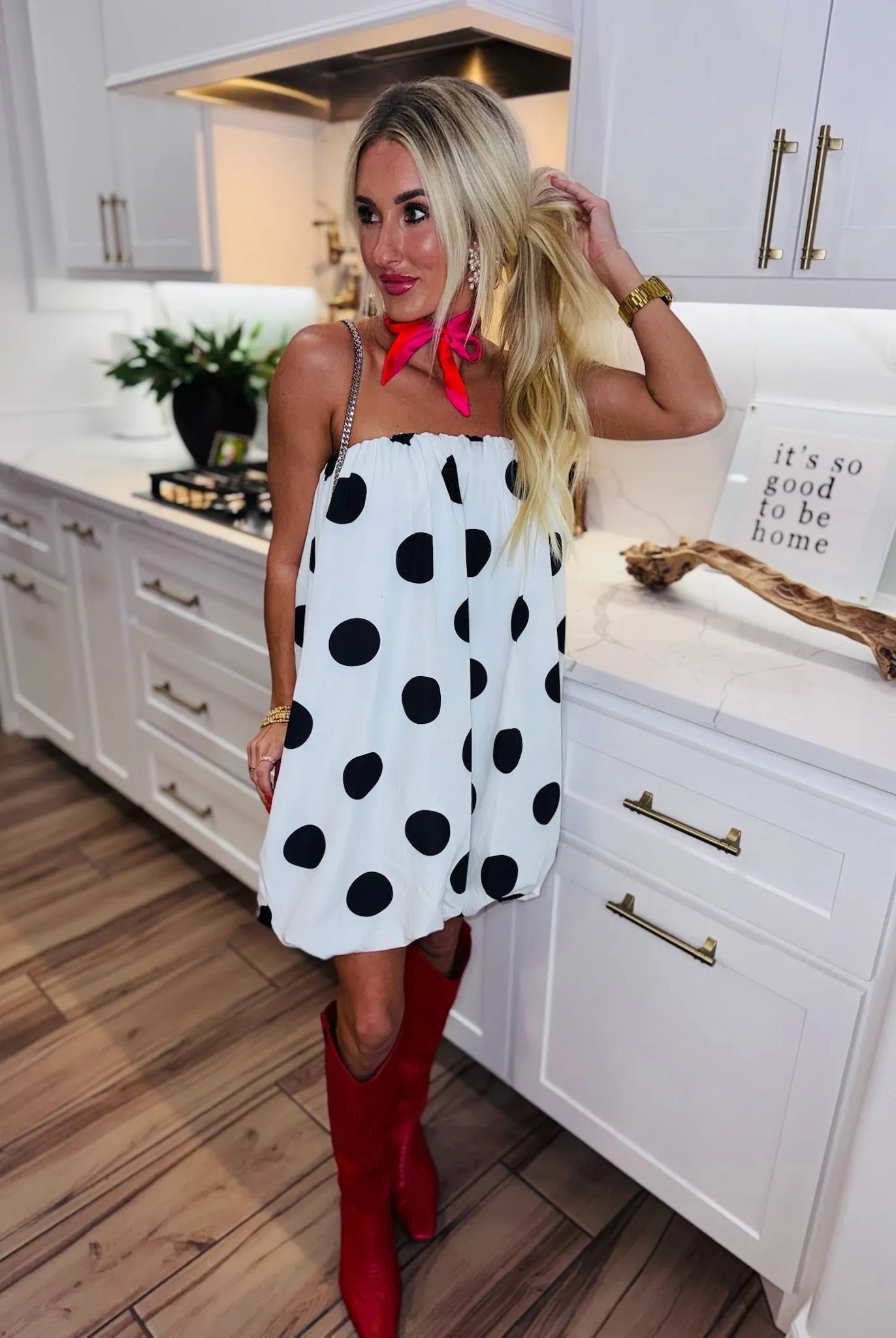Woman in white strapless bubble dress with black polka dots, red cowboy boots, and pink scarf.