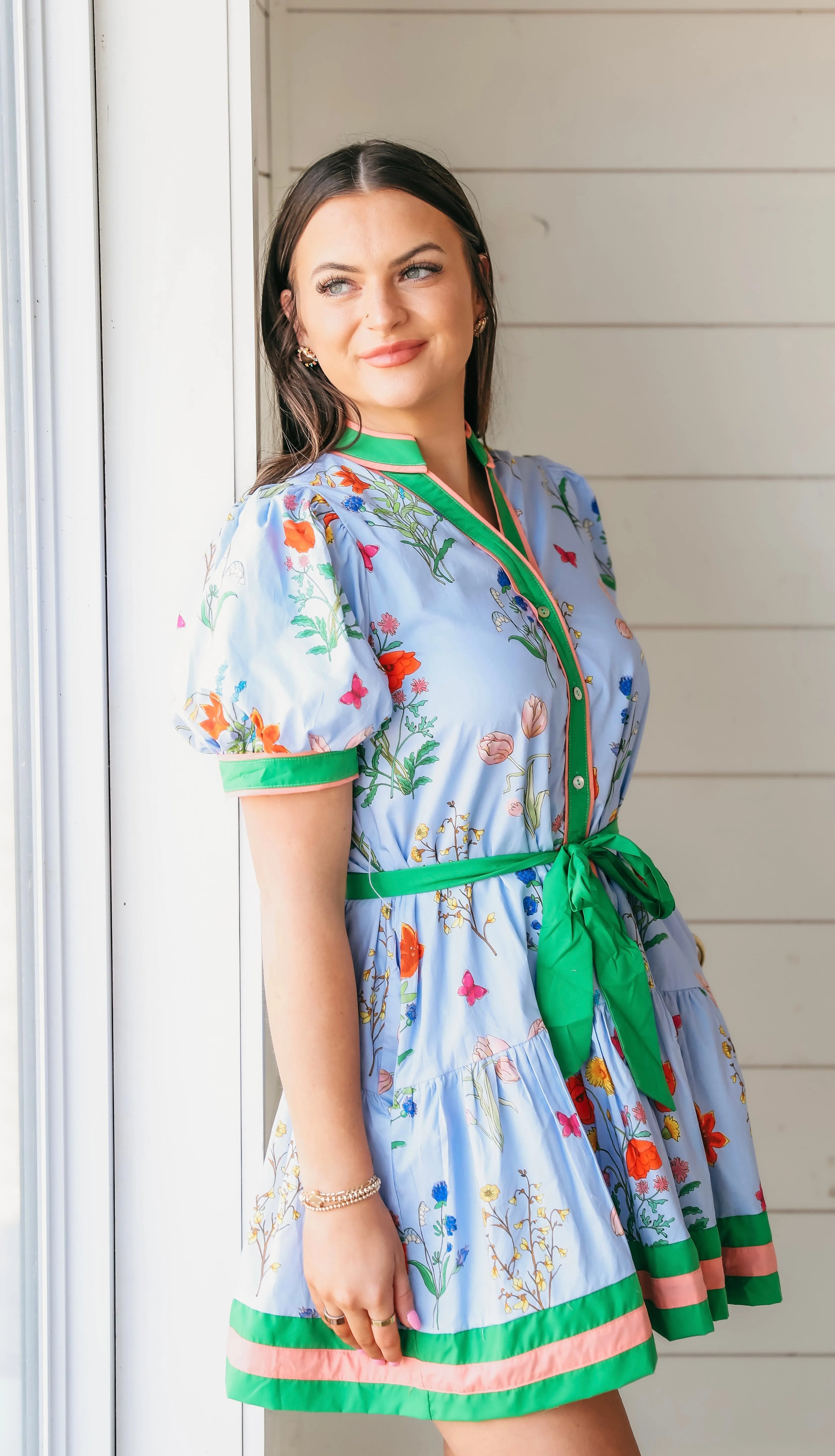 Blue button-down dress with a vibrant floral and butterfly print, puff sleeves, and a green tie belt. Features green and