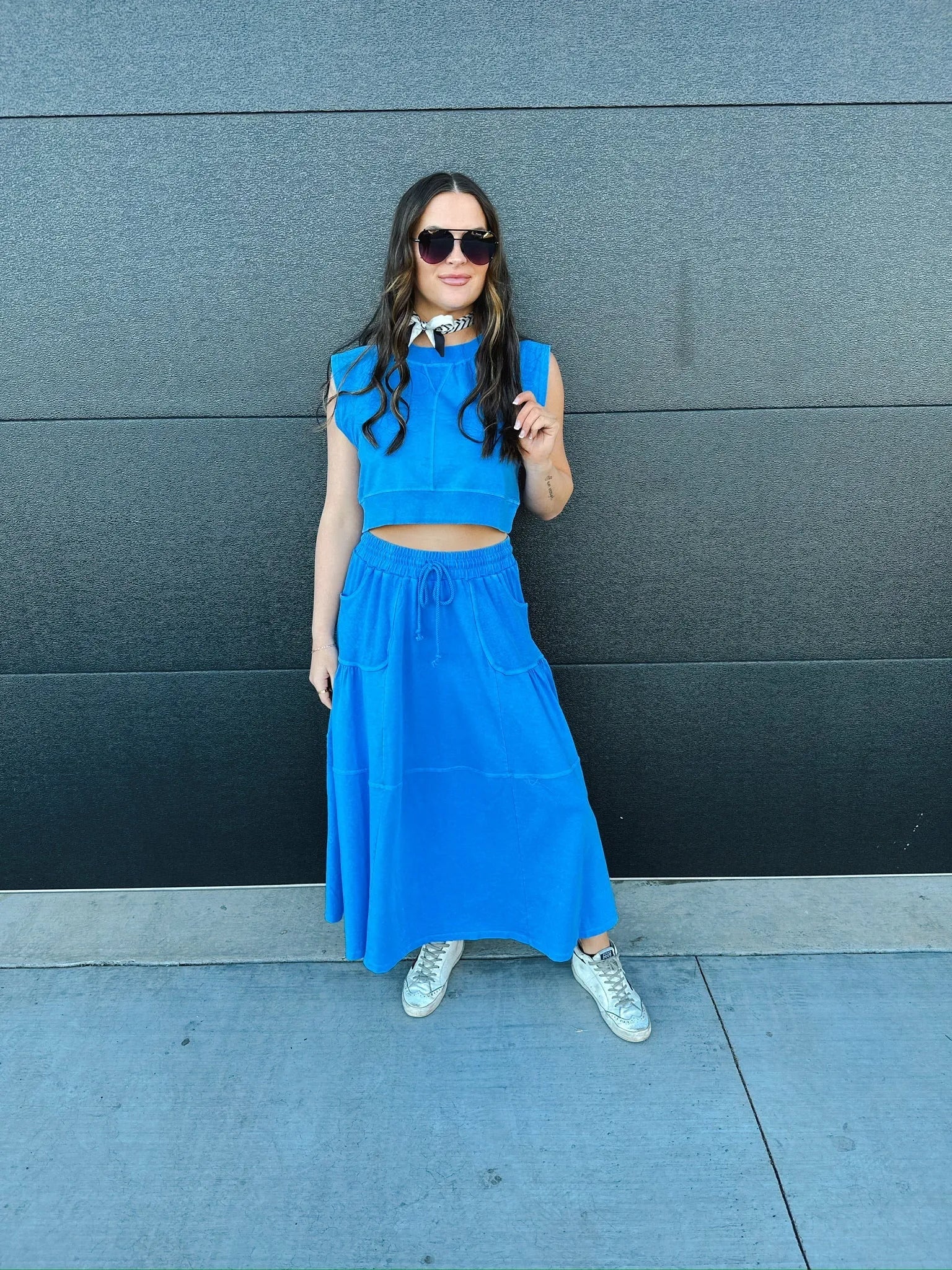 Blue sleeveless crop top and tiered maxi skirt set with drawstring waist. Model wears sunglasses and white sneakers.