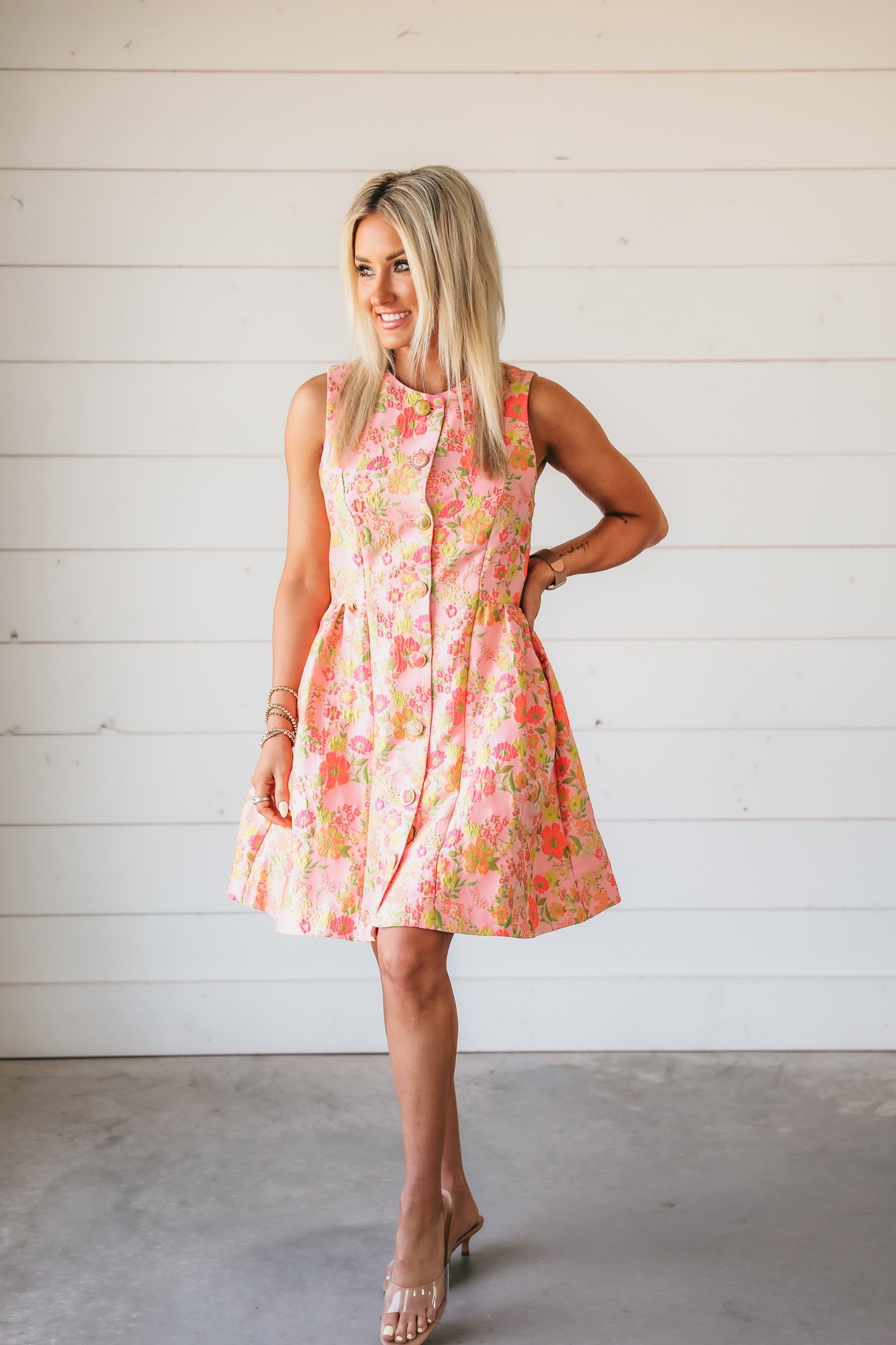 Bright pink brocade dress with vibrant floral print in coral, lime, and yellow. Sleeveless, A-line, button-front design.