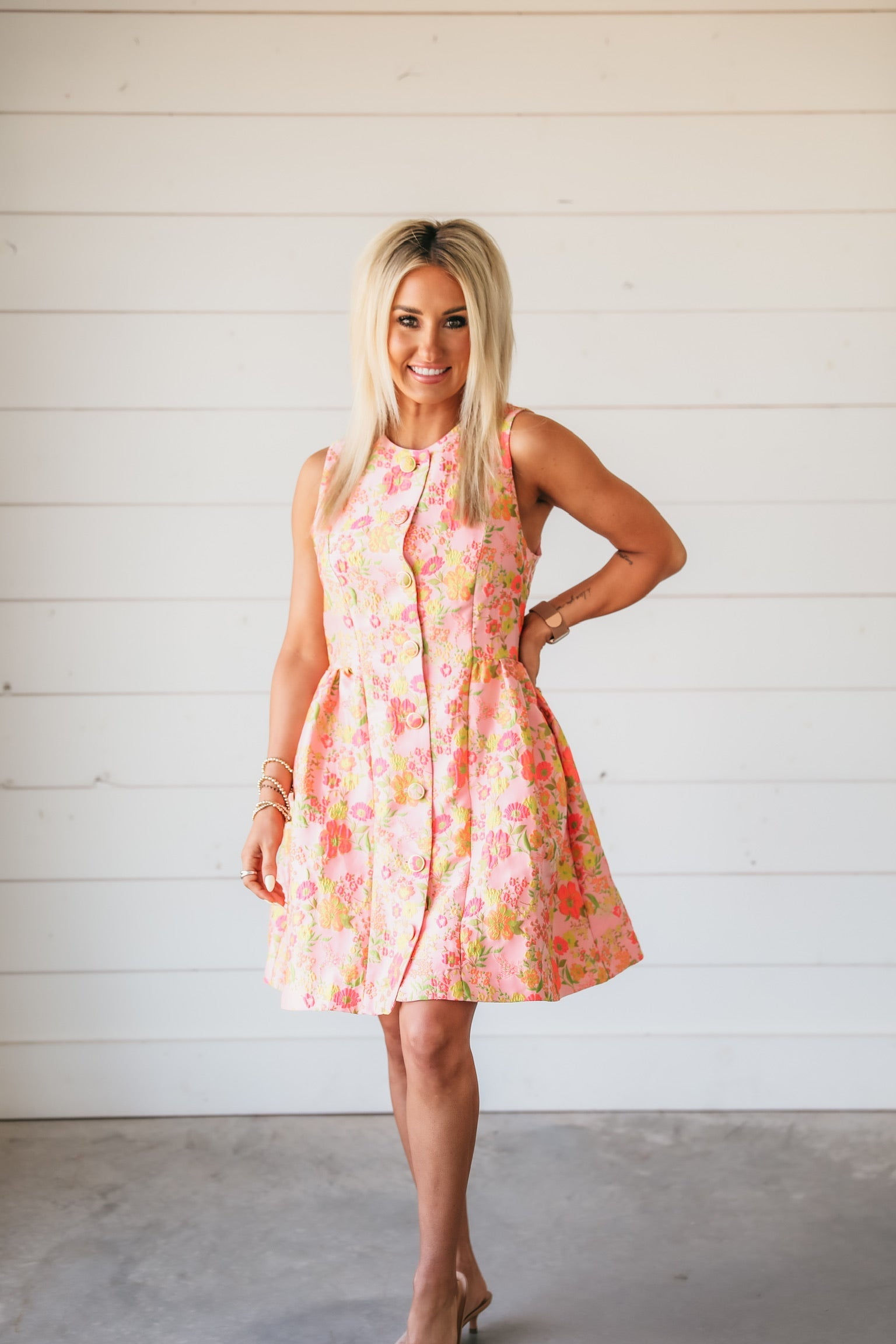 Woman in a pink floral brocade mini dress with lime and yellow accents and button front.