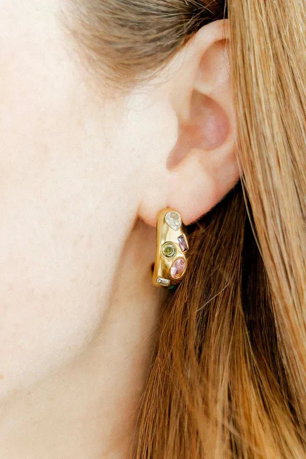 Close-up of a gold-plated hoop earring adorned with assorted colorful gemstones, including pink, green, and clear stones
