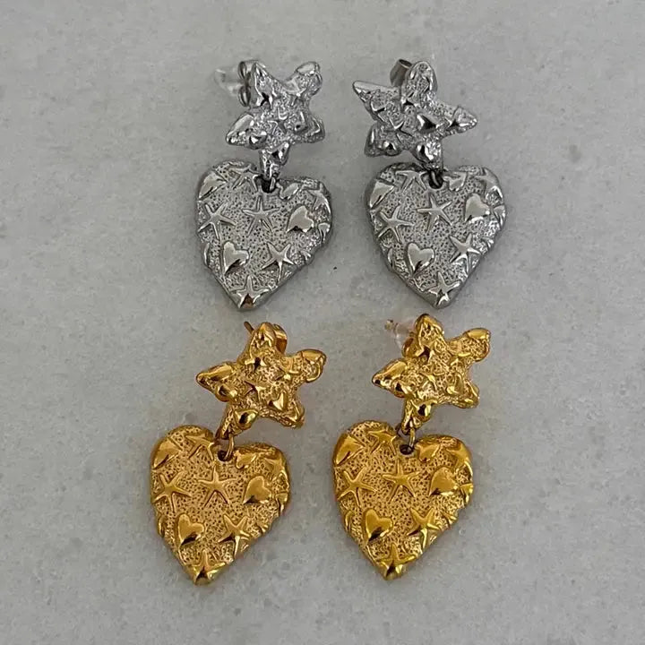 Two pairs of Caroline gold star heart drop earrings. One pair is silver-toned, the other gold-toned. Both feature textured
