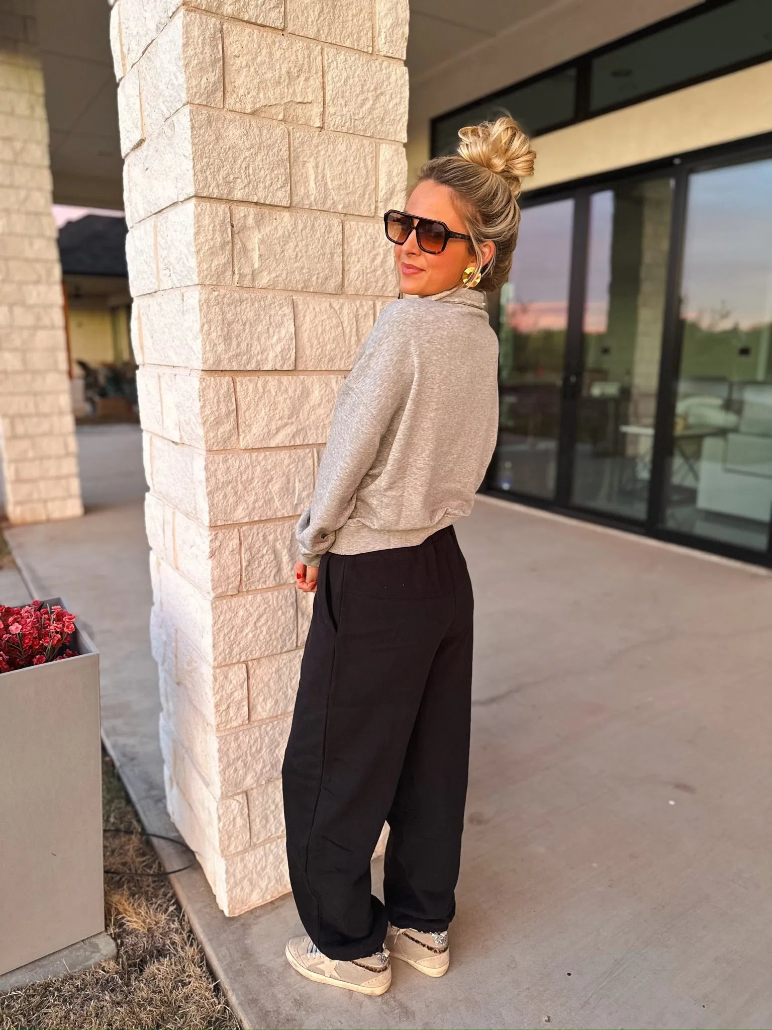 Woman wearing a grey collared half-zip sweatshirt with black pants, gold earrings, and sunglasses.