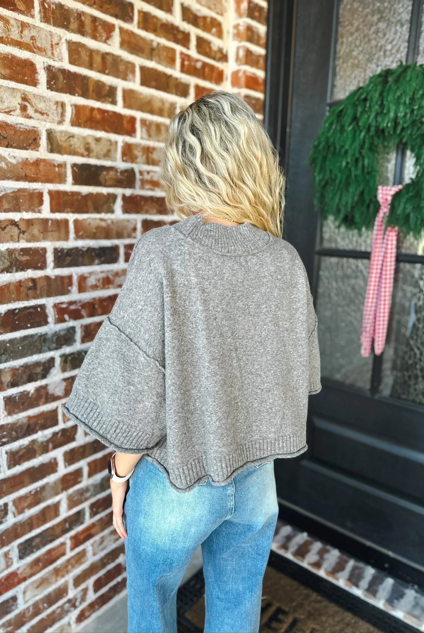 Woman wearing a charcoal brown soft knit sweater tee with wide short sleeves and a ribbed hem, paired with blue denim jeans.