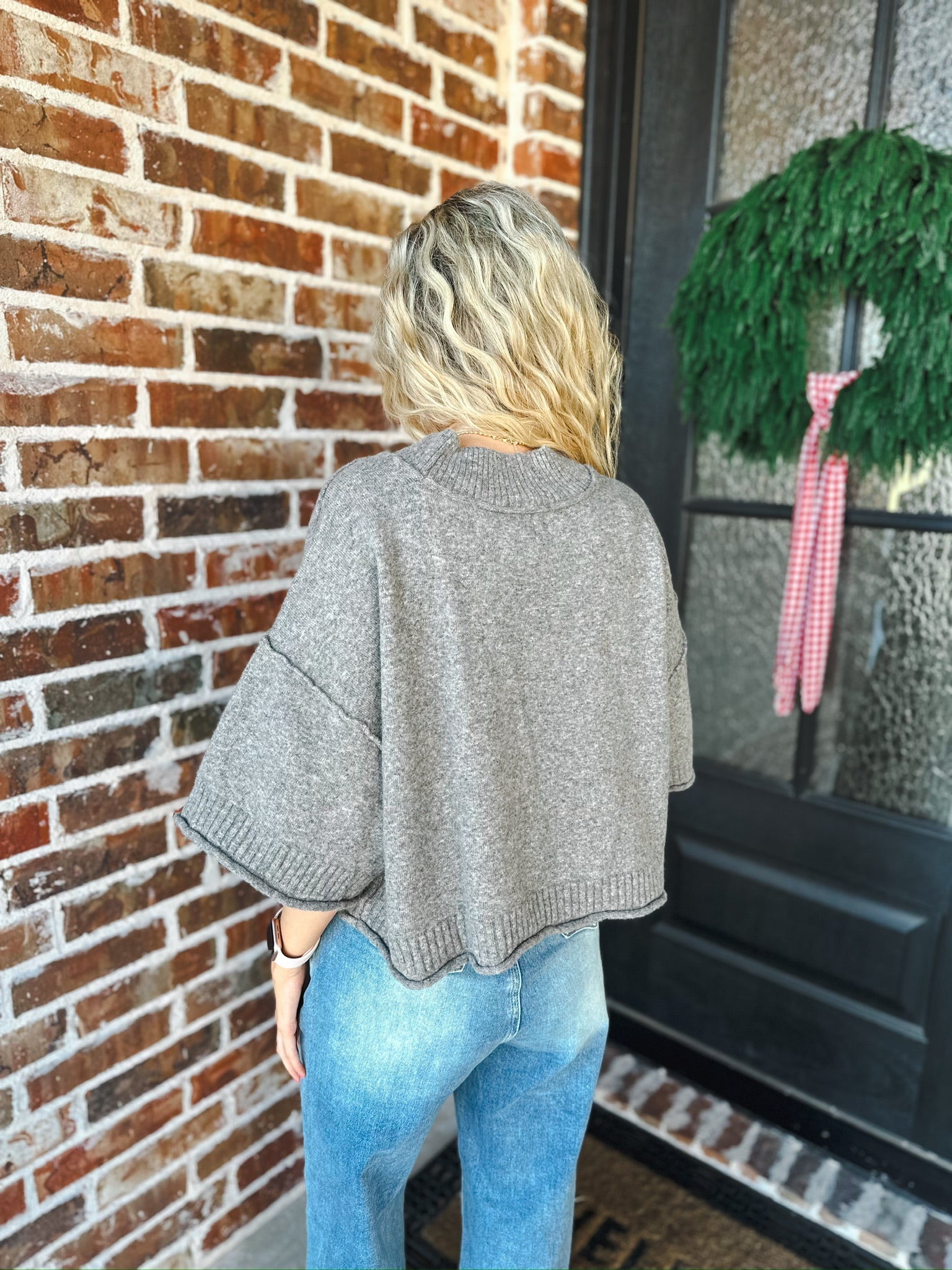 Woman wearing a charcoal brown soft knit sweater tee with wide short sleeves and a ribbed hem, paired with blue denim jeans.
