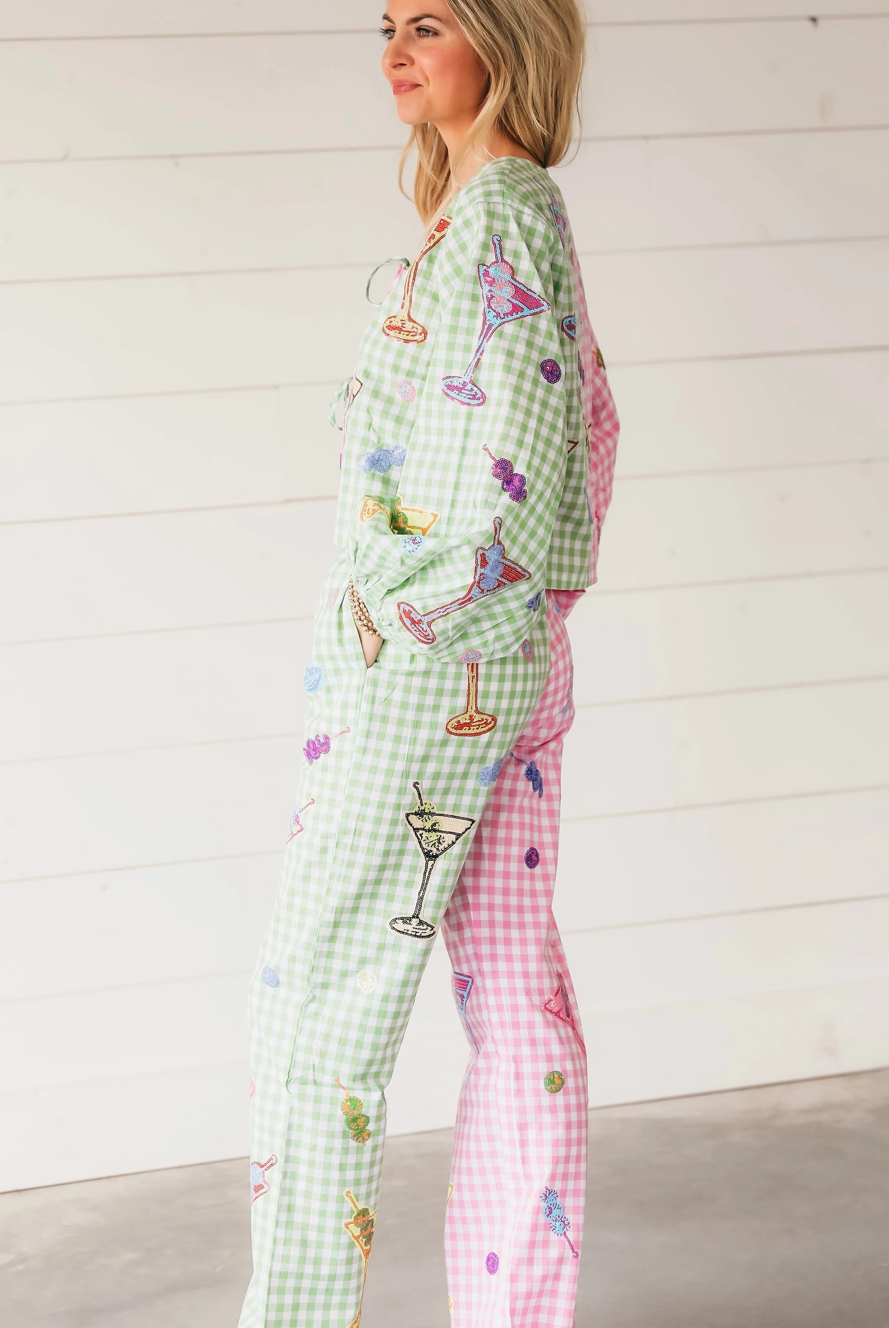 Woman wearing colorblock gingham Martini trousers, green and pink check with martini glass, fruit, and cocktail embroidery.