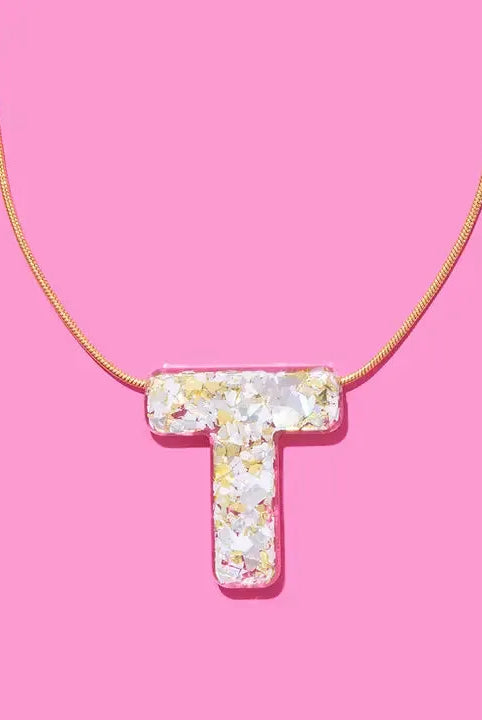 Gold chain necklace with a clear resin pendant shaped like the letter T, filled with white and gold confetti and glitter.