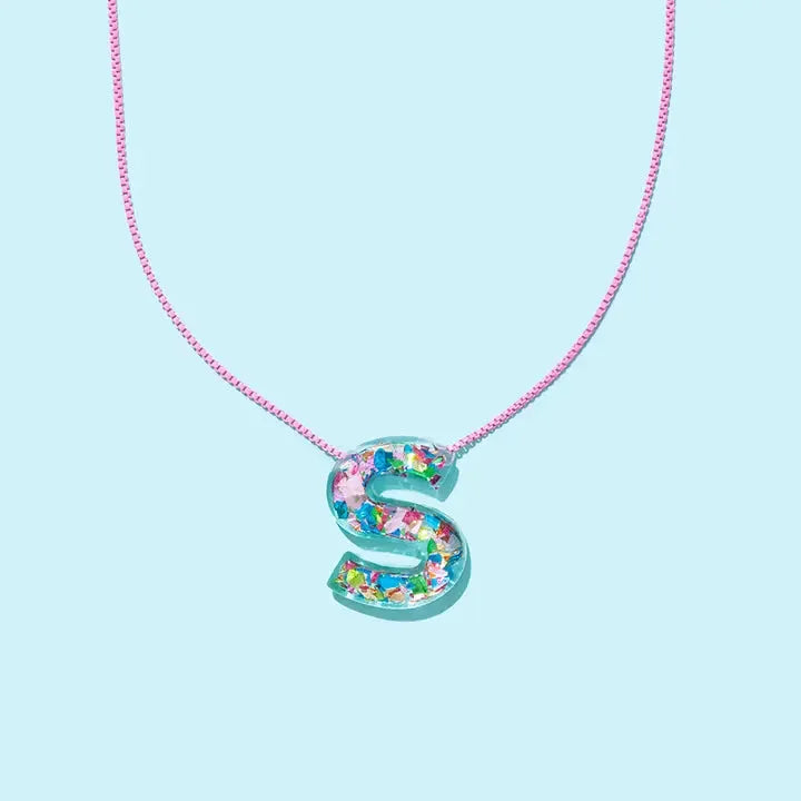 A clear resin letter S necklace filled with colorful confetti on a delicate pink chain against a light blue background.