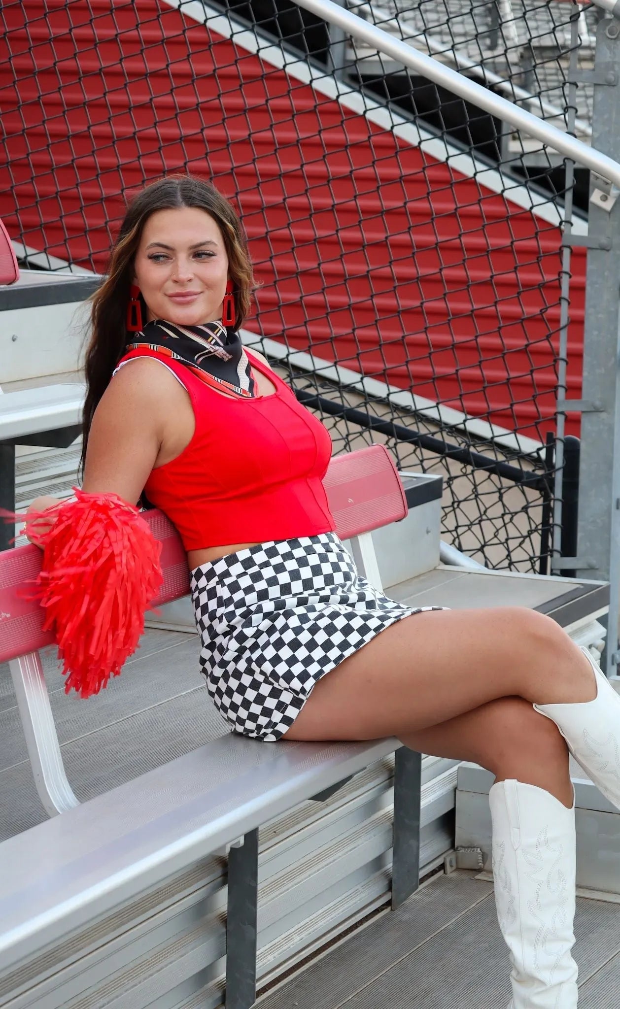 Woman wearing a red cropped tank top, black and white checkered mini skirt, and white cowboy boots, holding a red pom-pom.