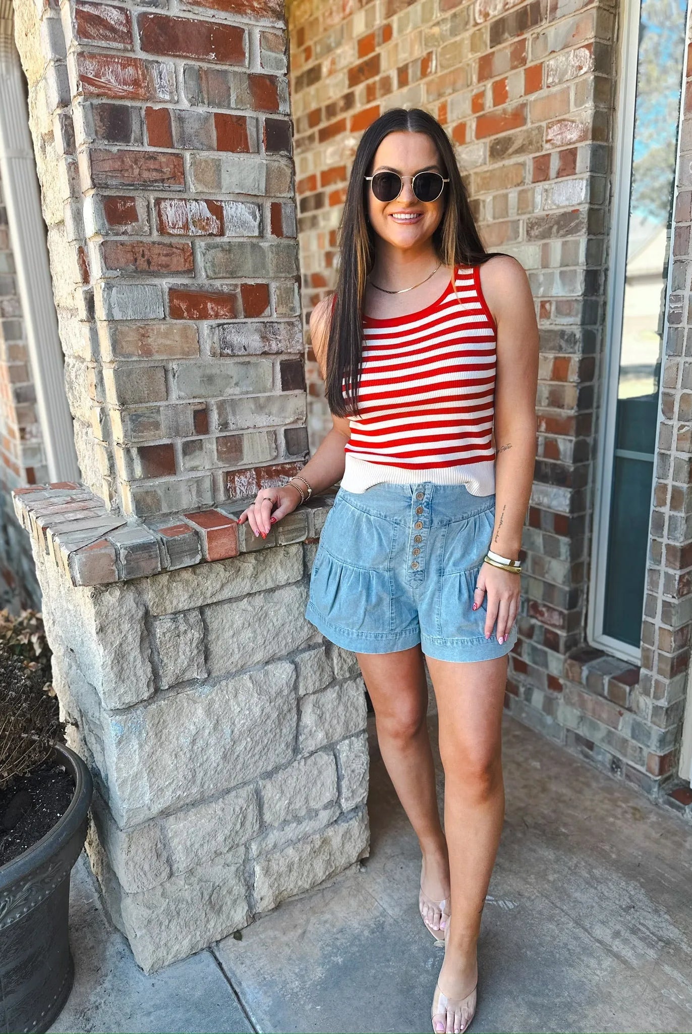 Woman wearing a cream and red striped tank top with a white hem and light blue denim ruffled shorts with a button-up front.